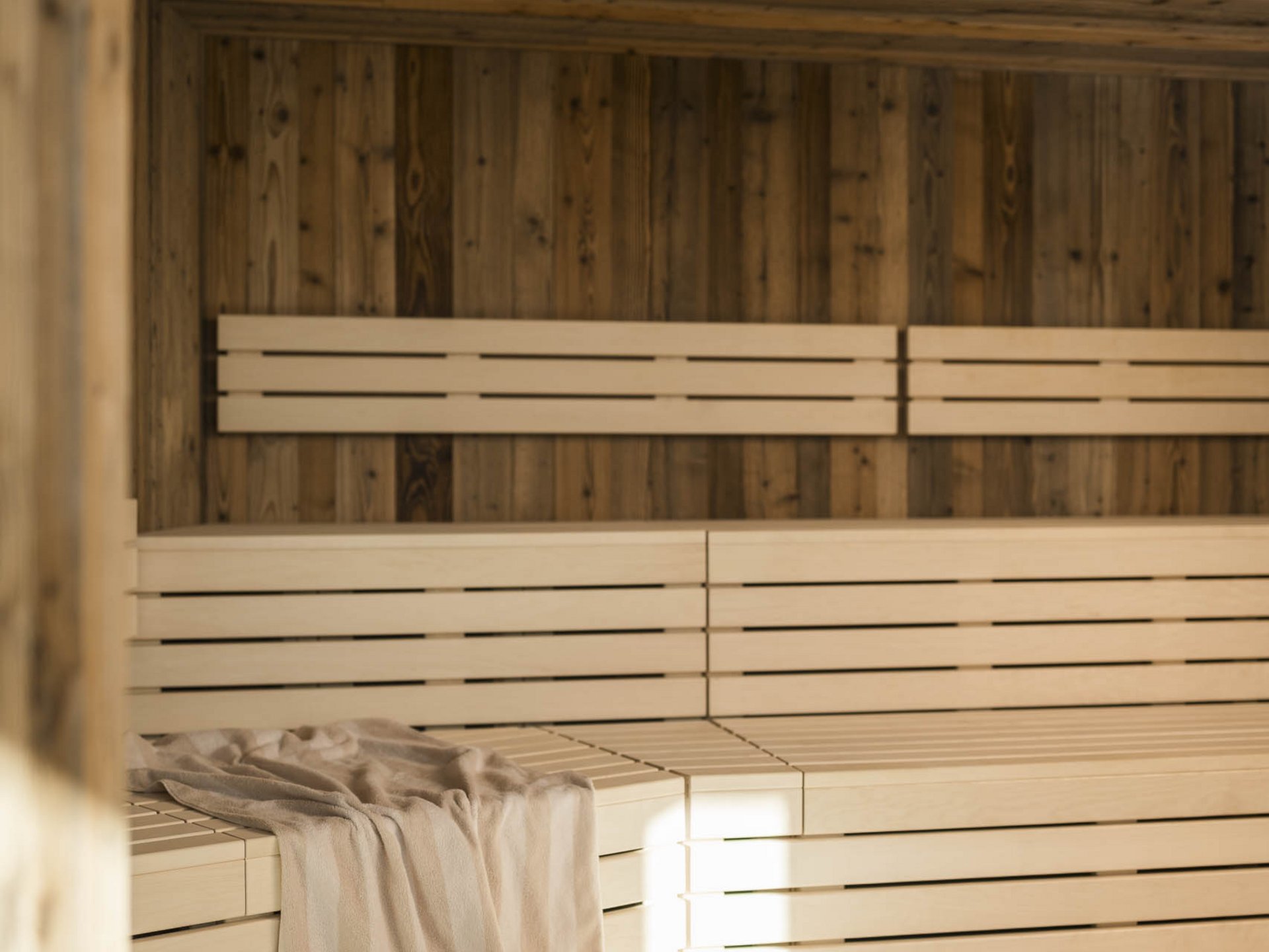 Innenansicht einer hellen Sauna mit Holzvertäfelung und Handtuch auf der Bank