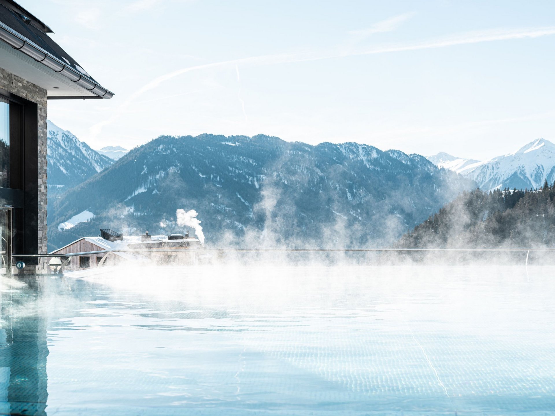 Steaming infinity pool with mountain and snow-covered peaks in background