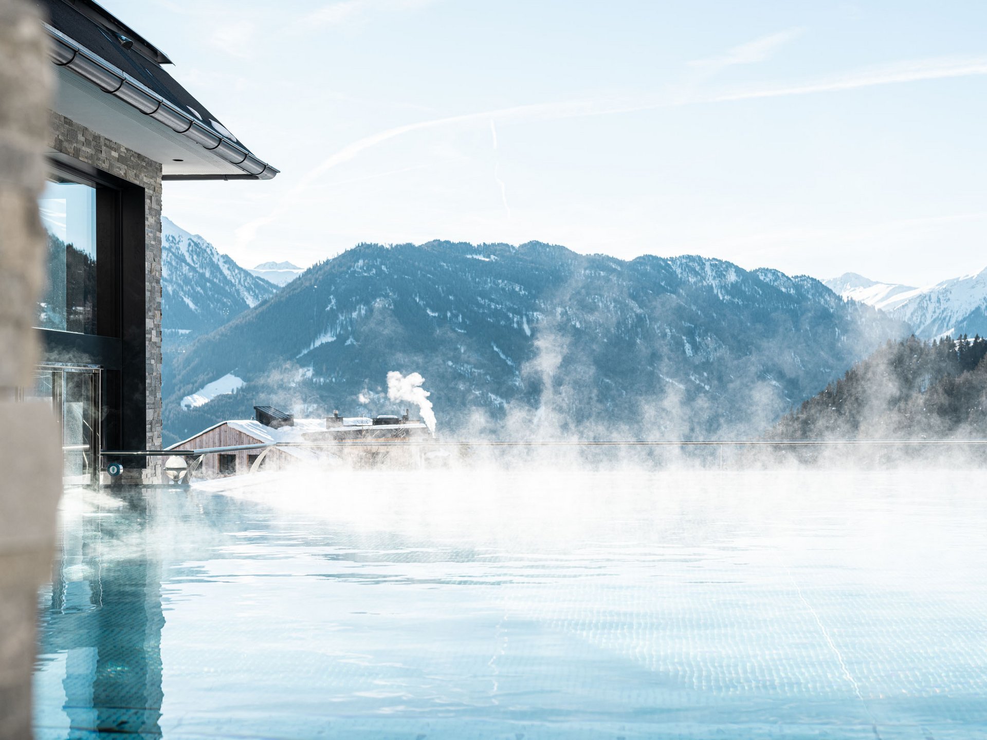 Steaming infinity pool with mountain and snow-covered peaks in background