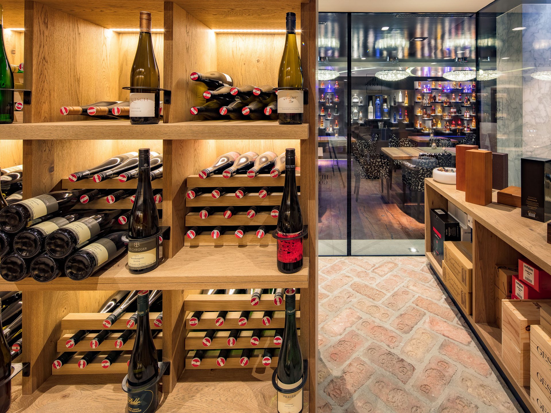 Wine cellar with wooden shelves and bar visible through glass in background