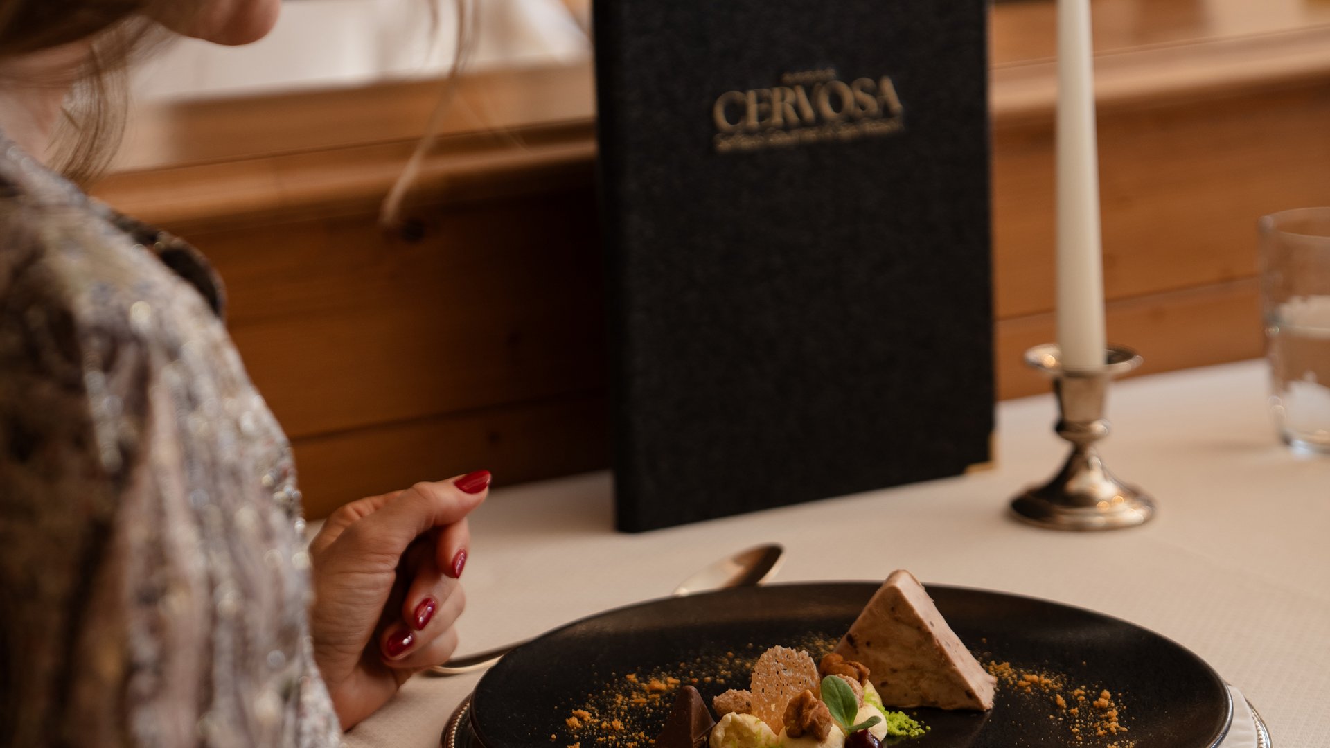 Woman sitting at table with dessert, lit candle, and menu card