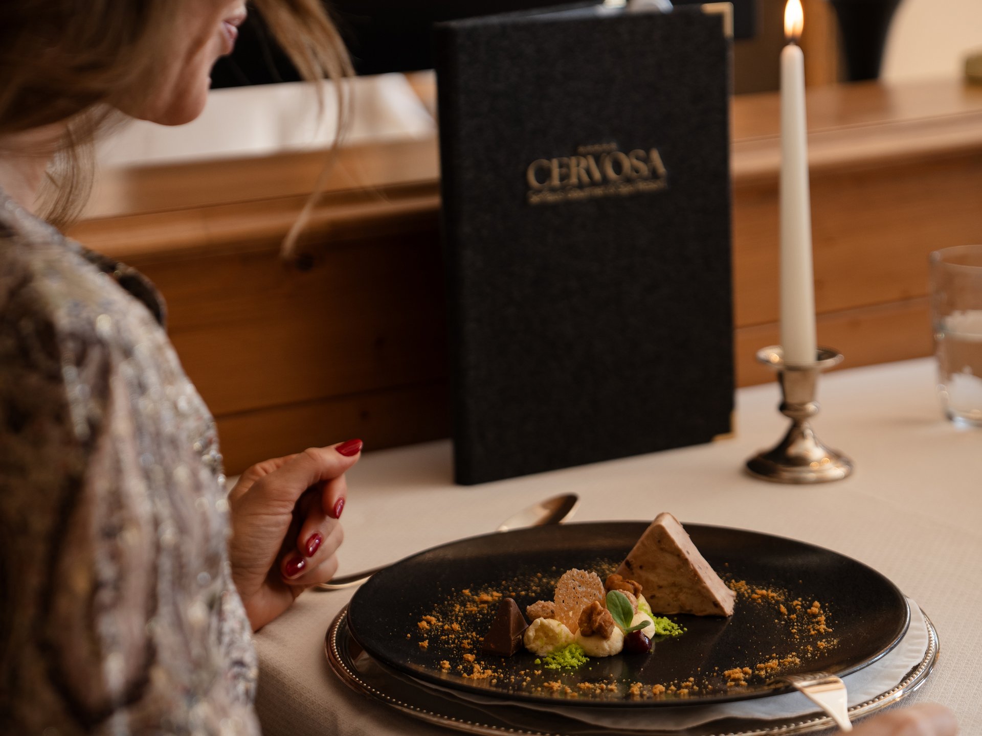 Der Gipfel des Geschmacks im Gourmethotel in Tirol Frau sitzt am gedeckten Tisch mit Dessert, Kerze und Menükarte