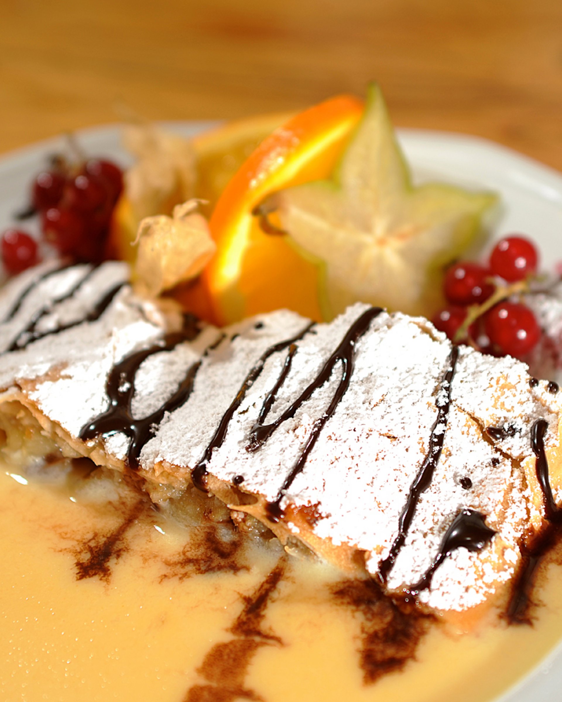 Die Cervosa Alm auf 2 000 Metern Apfelstrudel mit Vanillesoße, Puderzucker und frischen Früchten auf weißem Teller