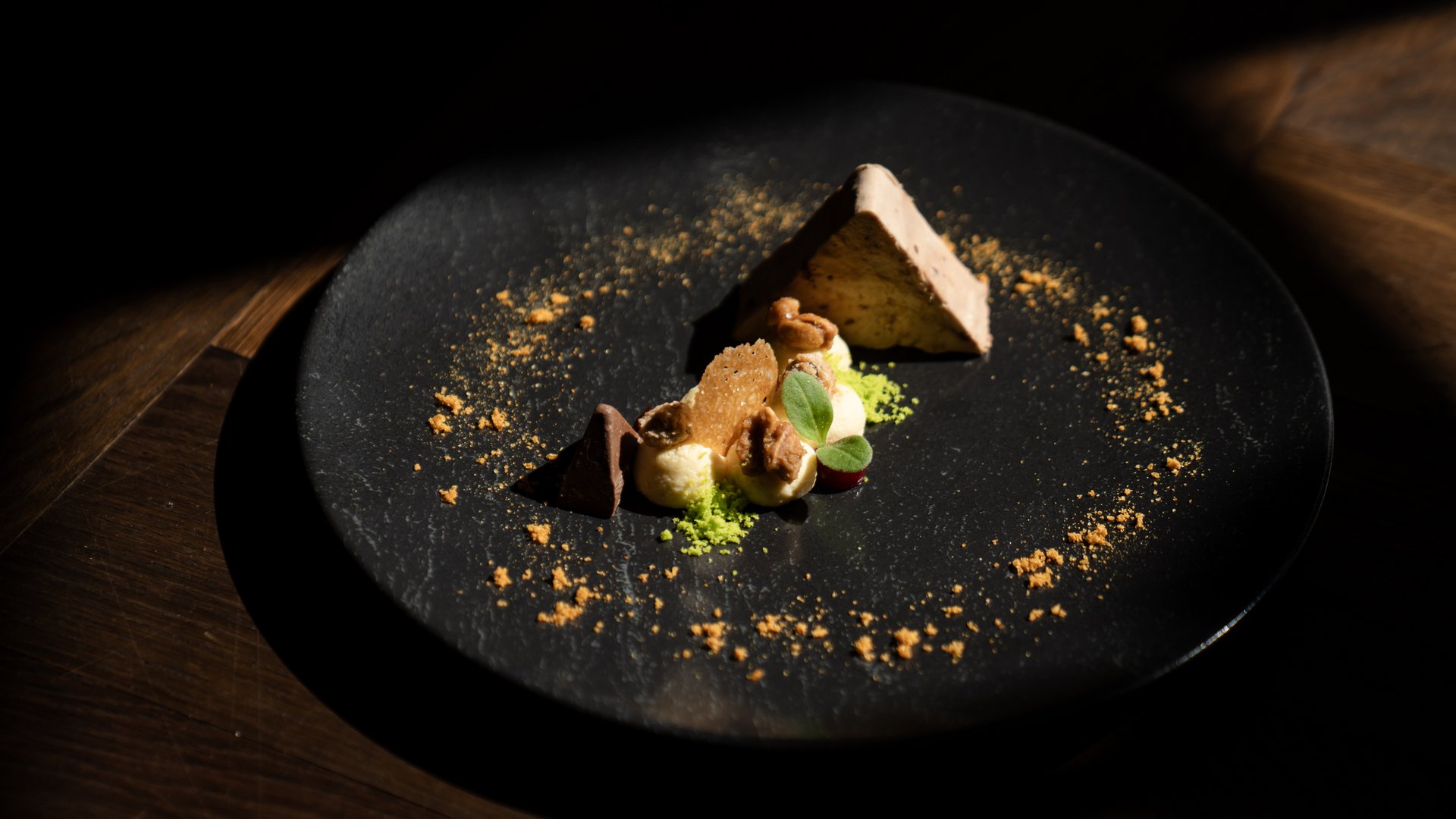 Creative dessert with cream, nuts, and chocolate pieces on black plate