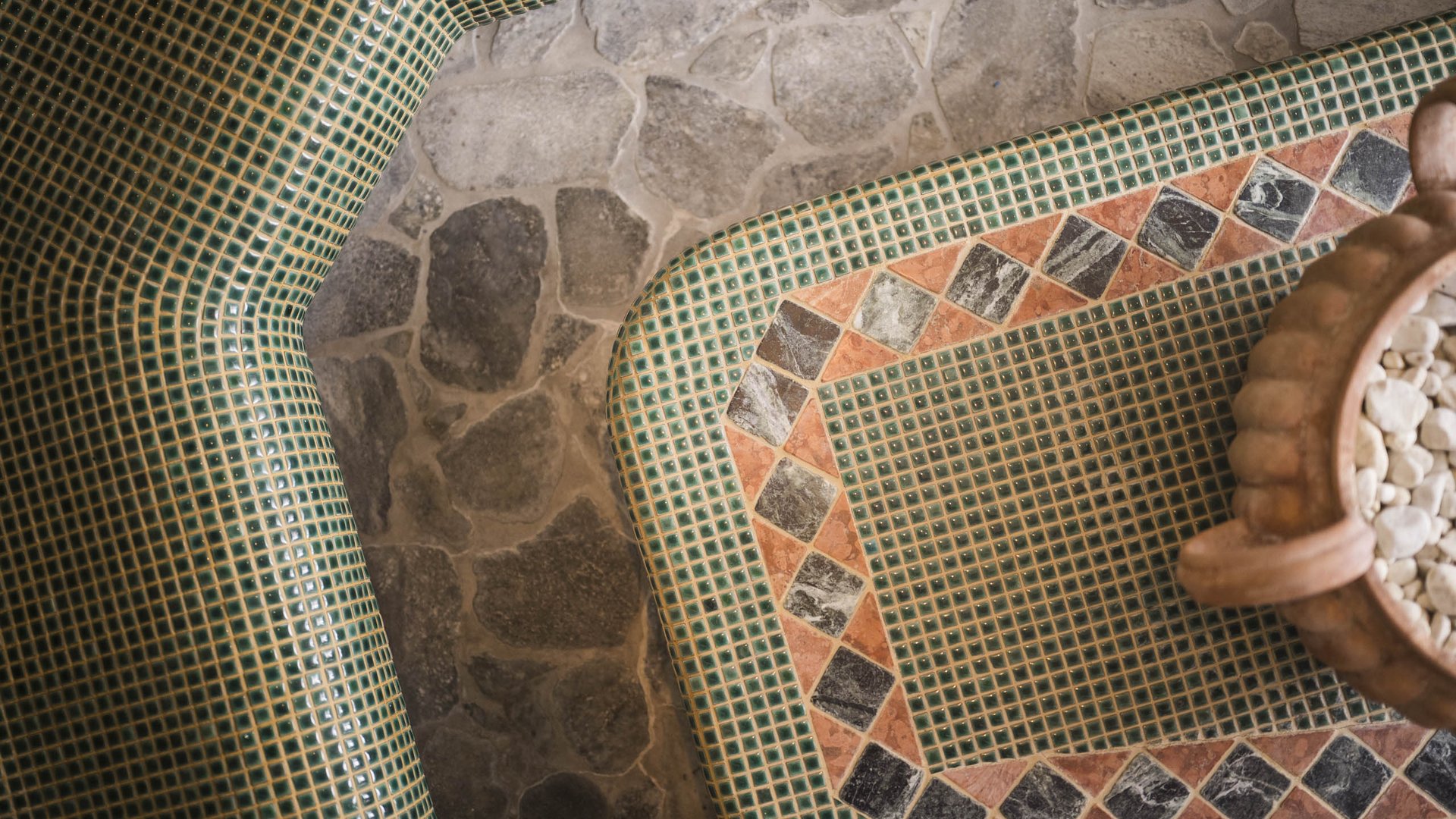 Green and orange mosaic tiles with stone floor and decorative vase