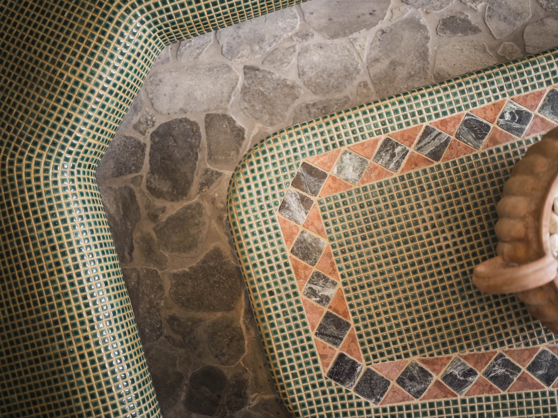 Green and orange mosaic tiles with stone floor and decorative vase