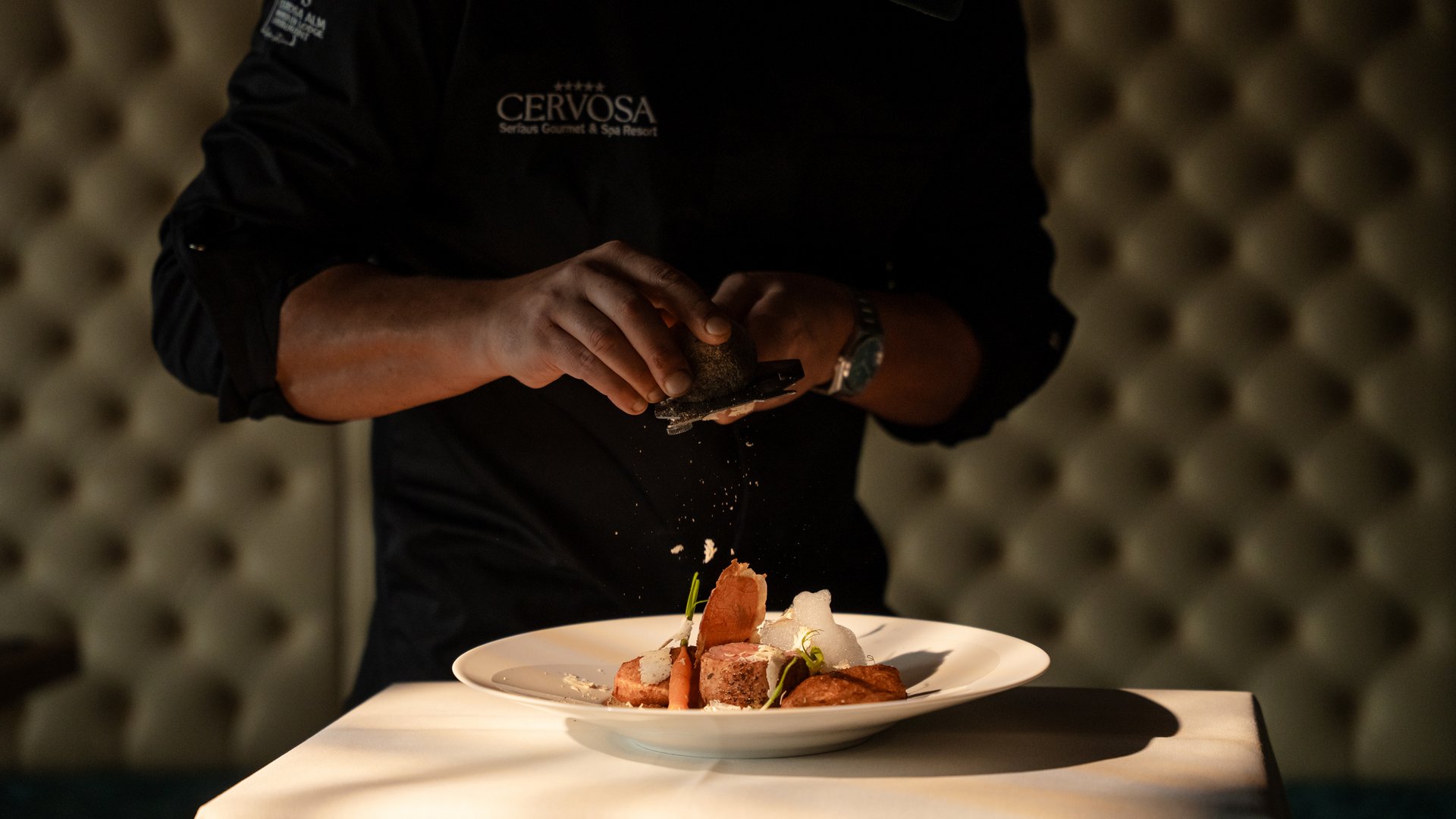 Chef artistically seasoning a dish on a white plate in a restaurant