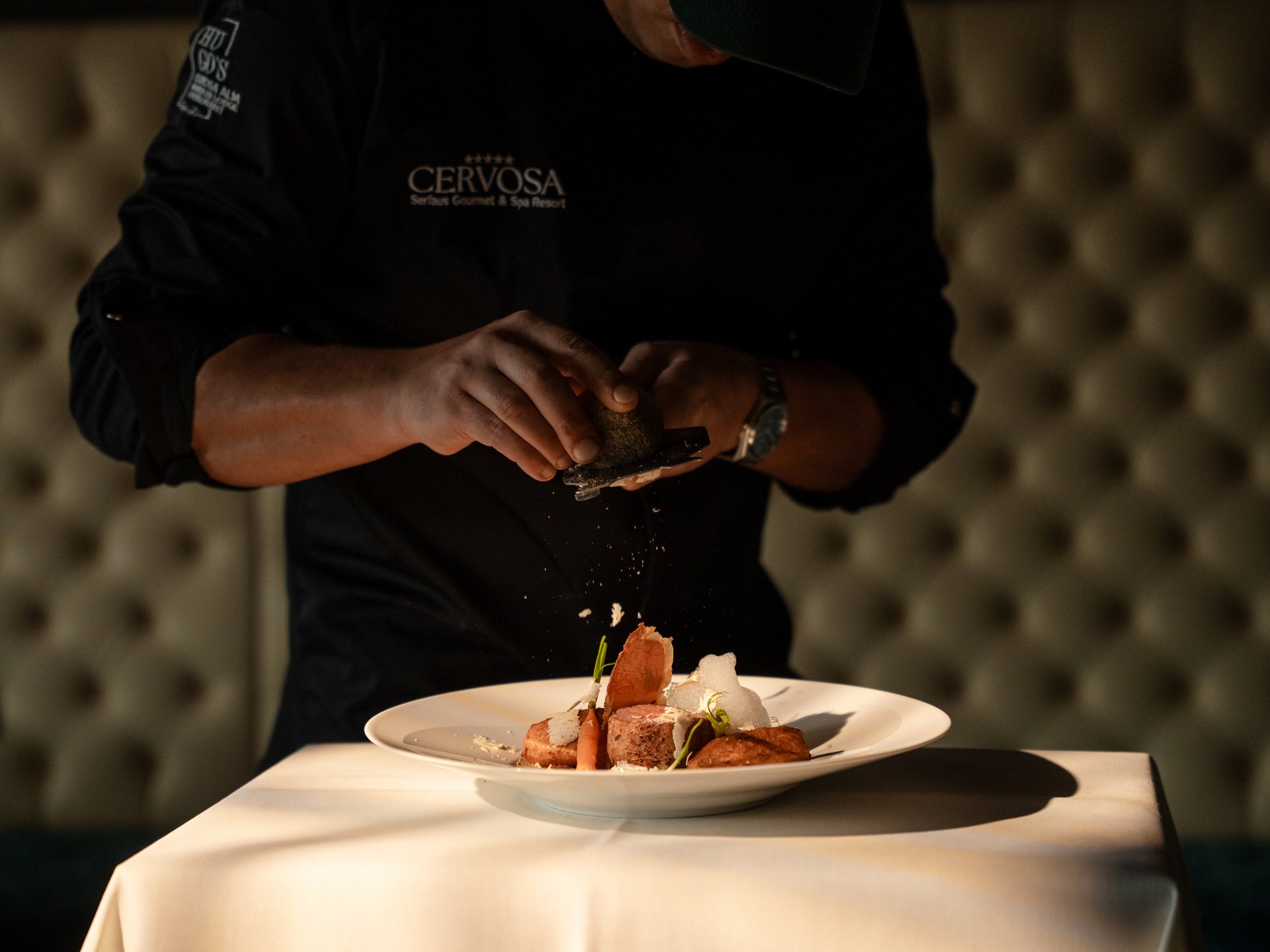 Savour the mountain flavours at our gourmet hotel in Tyrol Chef artistically seasoning a dish on a white plate in a restaurant
