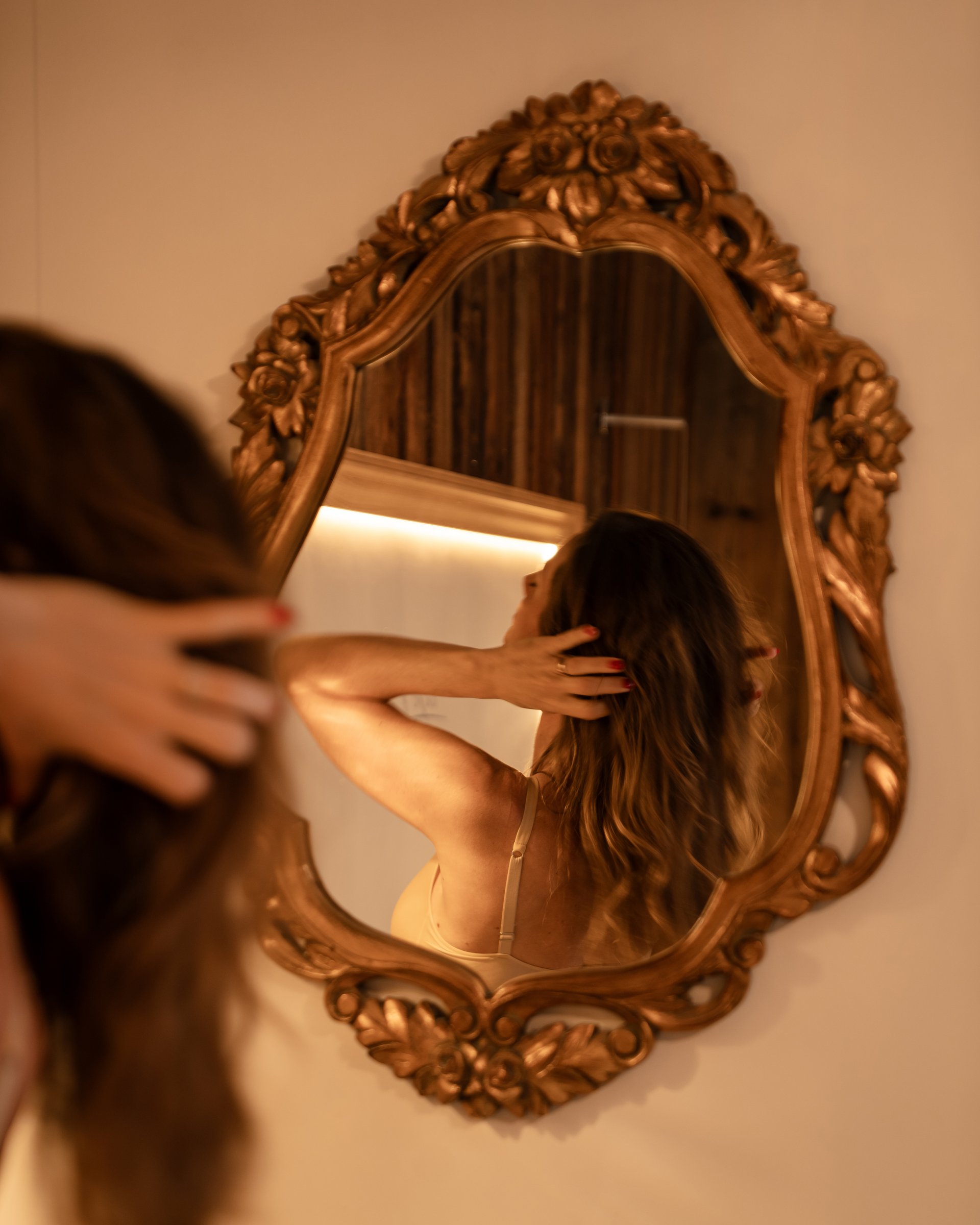 Feel-good holiday at our 5-star hotel in Serfaus Woman looking at herself in an ornate wall mirror touching her hair