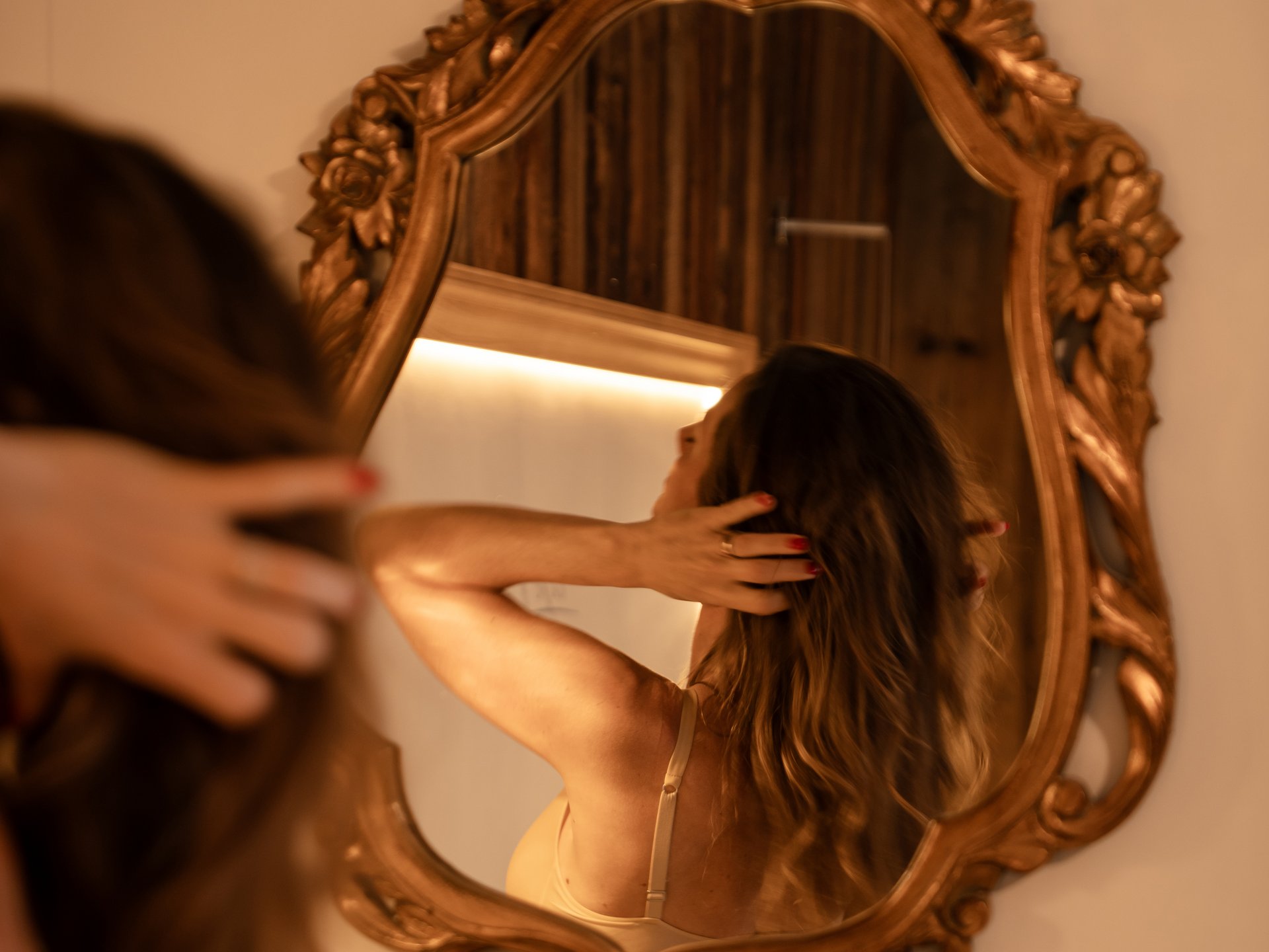 Frau betrachtet sich im verzierten Wandspiegel und berührt ihr Haar