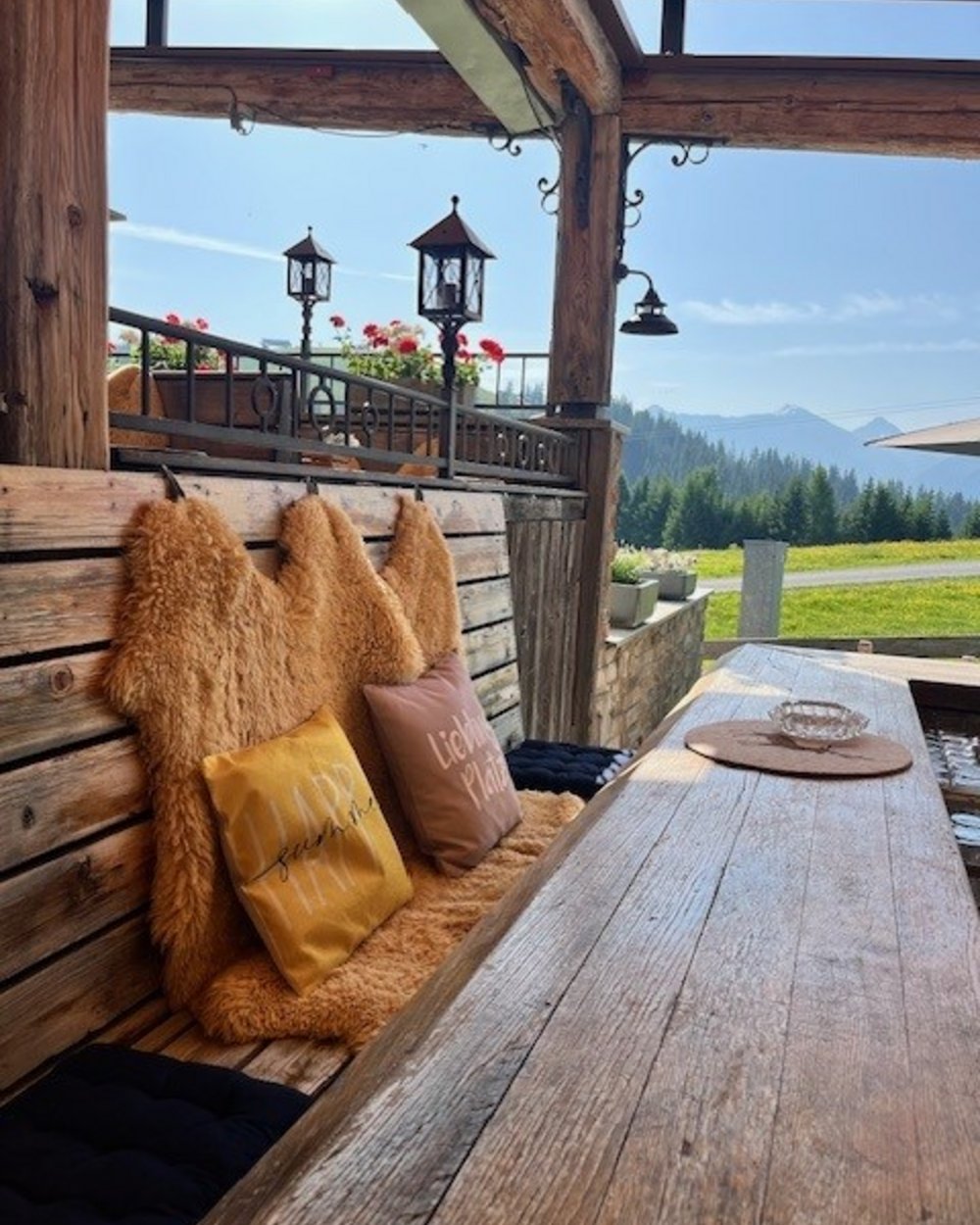 Rustikale Holzbänke mit Fellauflagen und Kissen auf einer Terrasse mit Bergblick