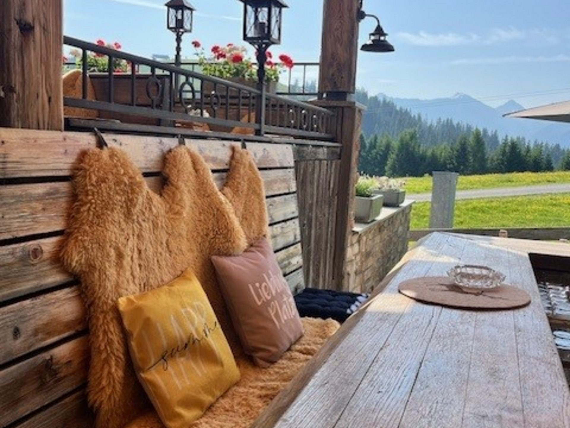 Die Cervosa Alm auf 2 000 Metern Rustikale Holzbänke mit Fellauflagen und Kissen auf einer Terrasse mit Bergblick