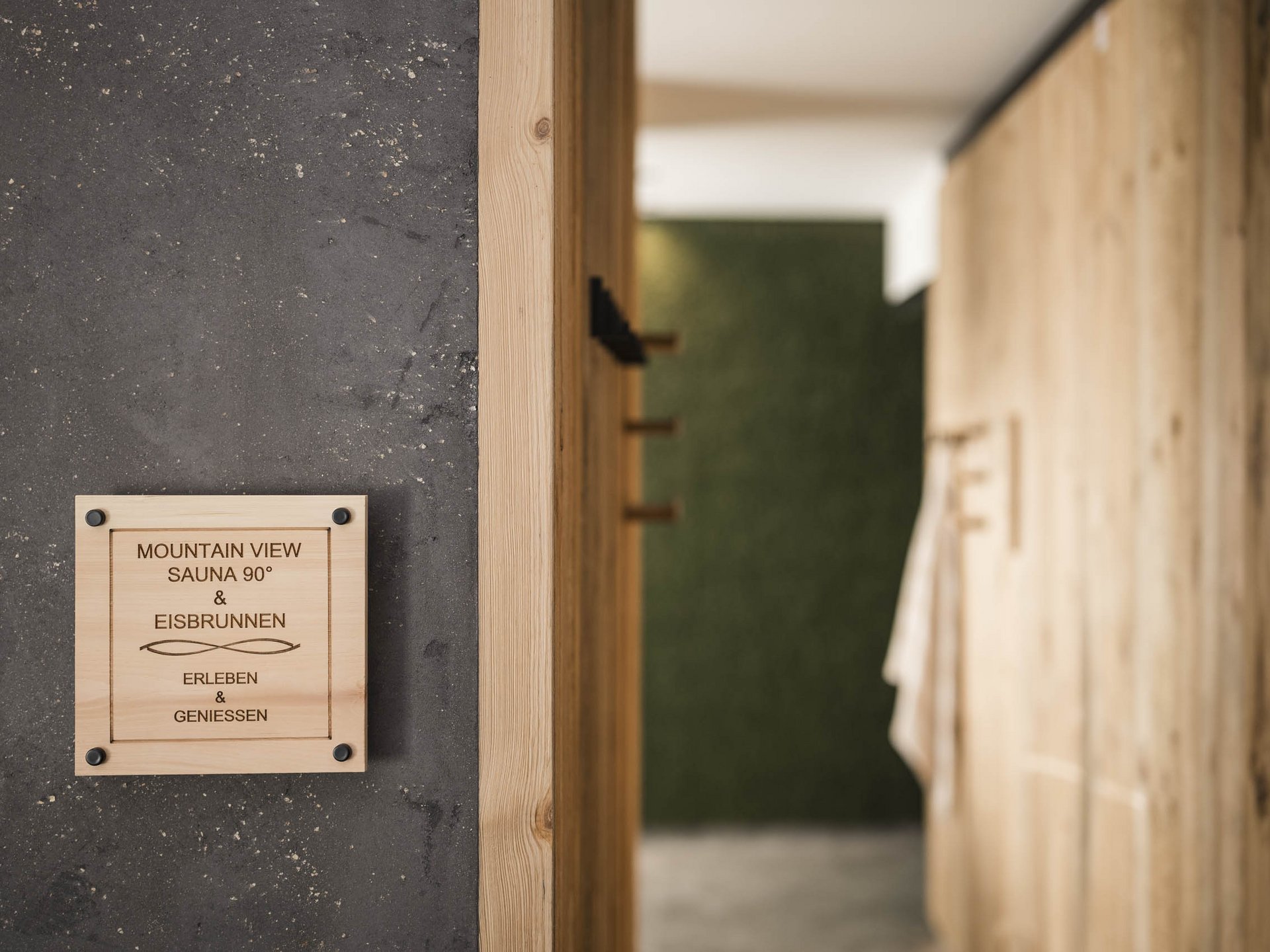 Holzschild mit Sauna- und Eisbrunnen-Hinweis an dunkler Wand neben Holzspinden