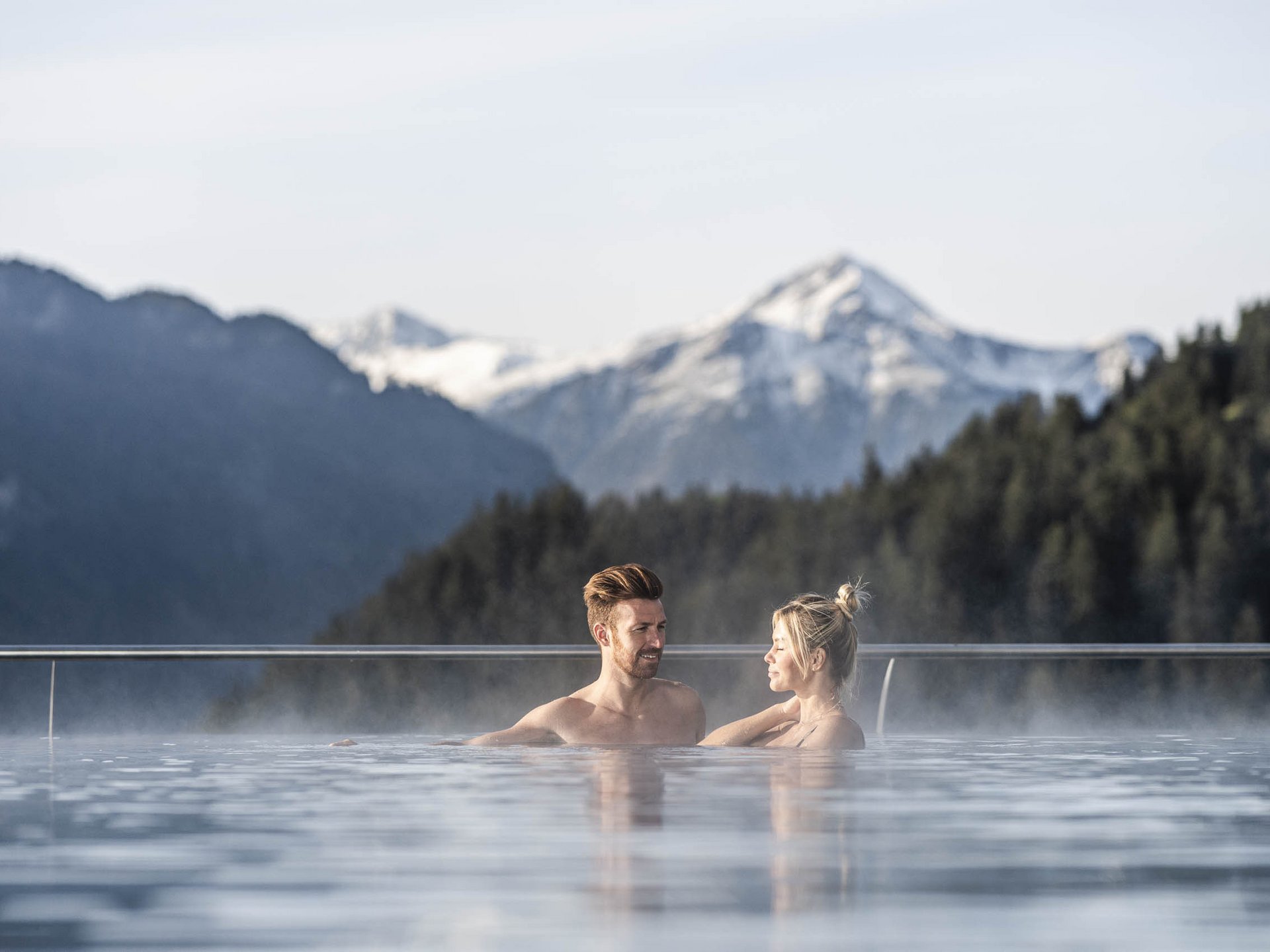 Couple relaxing in outdoor pool with mountain view and steam rising from water