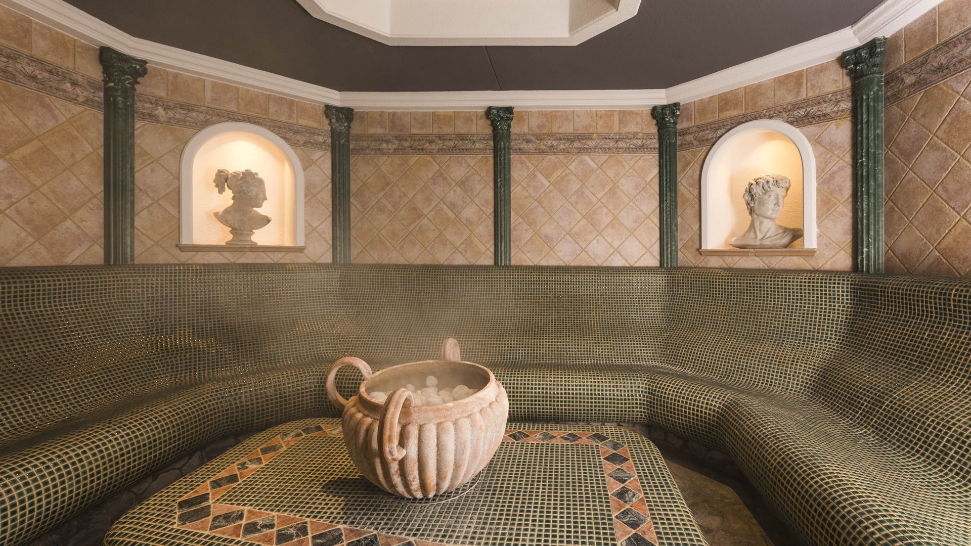 Roman steam bath with mosaic bench, stone amphora, and busts in niches