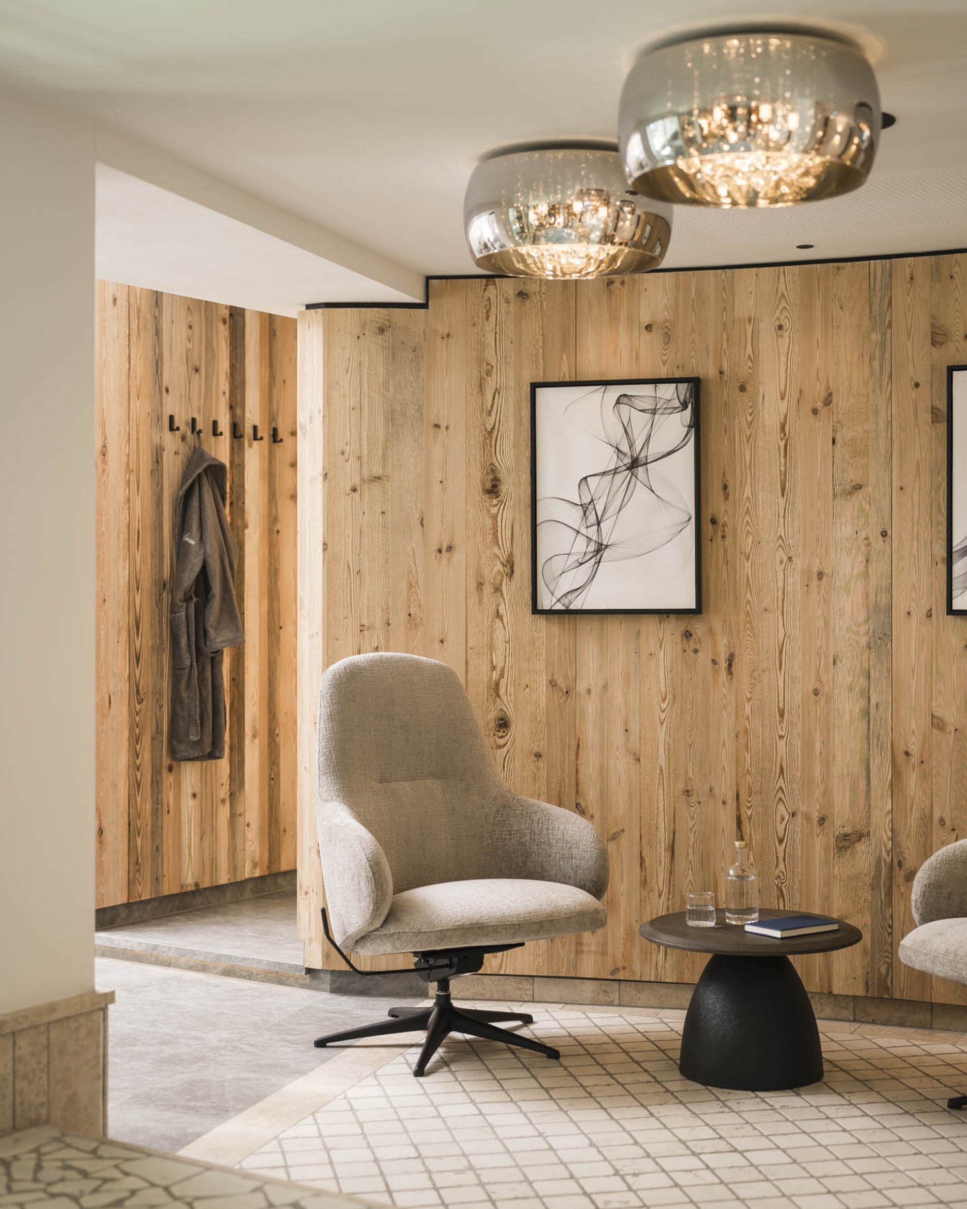Modern seating area with two gray armchairs, small table, and wood-paneled wall