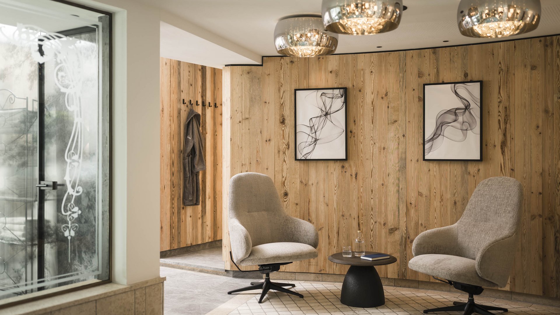 Modern seating area with two gray armchairs, small table, and wood-paneled wall