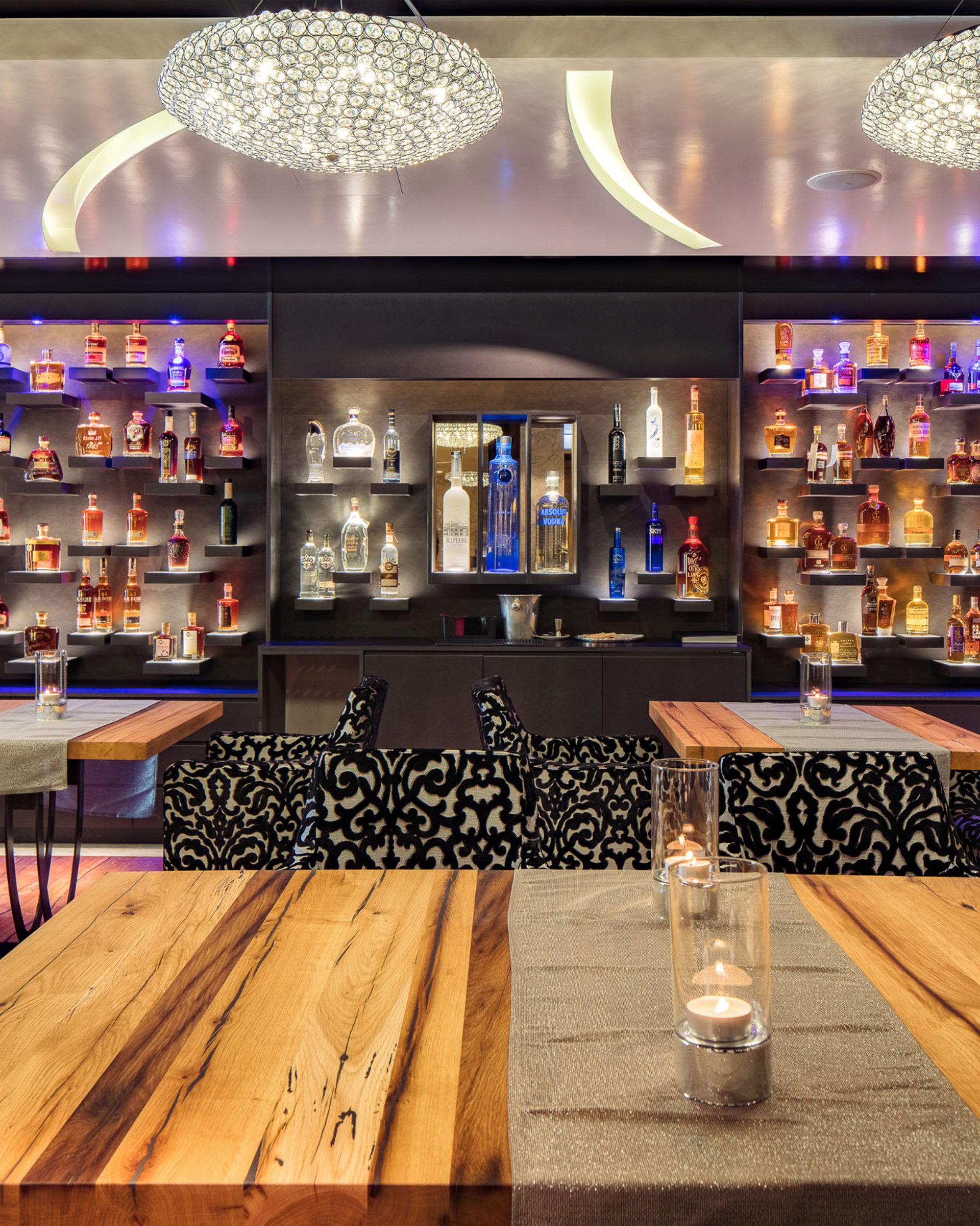 Moderne Bar mit beleuchteten Regalen voll Spirituosen und verzierten Sesseln