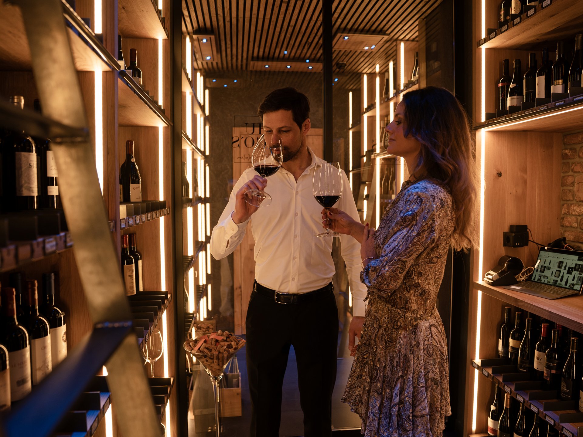 Couple tasting wine in a modern wine cellar with wooden shelves and warm lighting