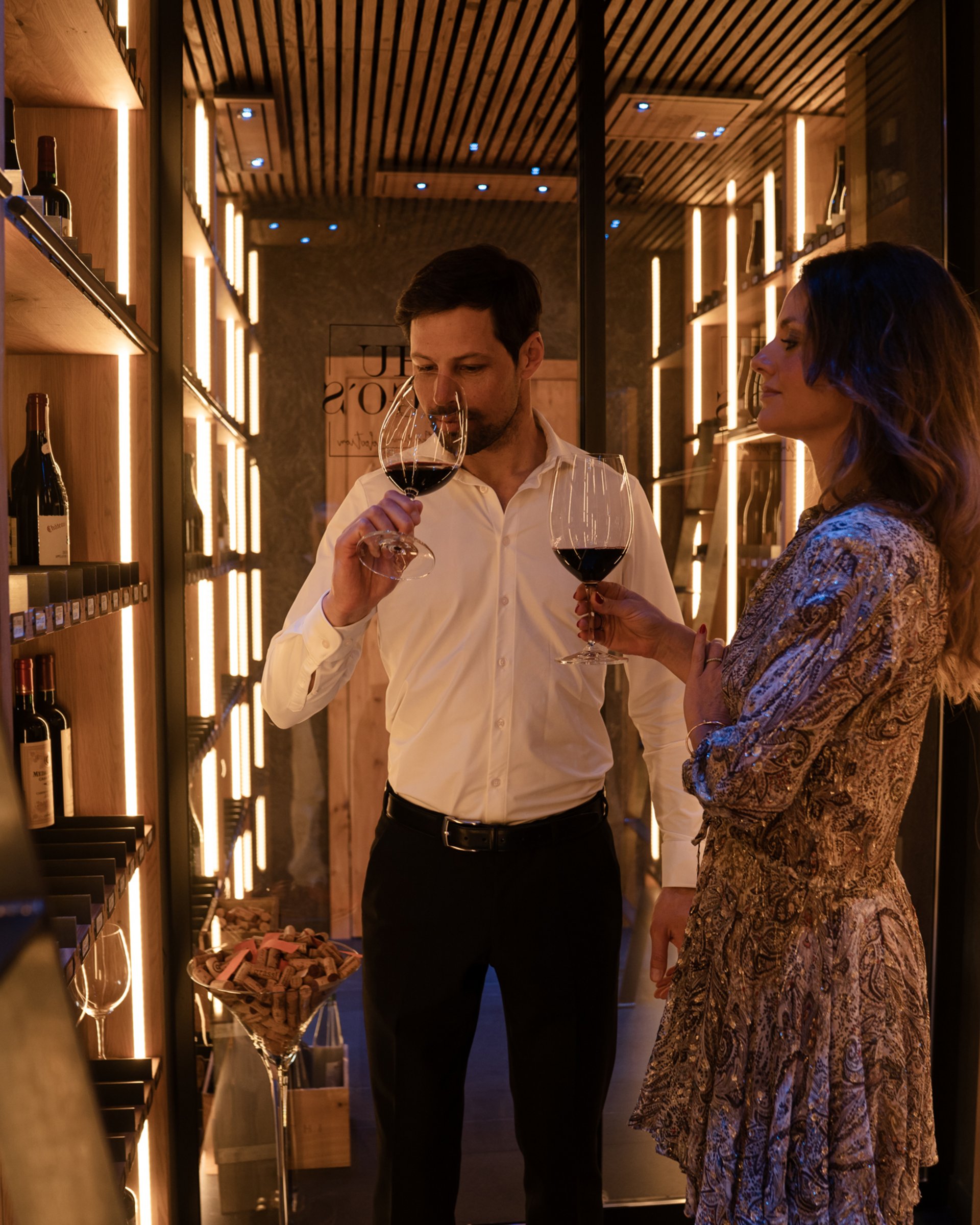 Couple tasting wine in a modern wine cellar with wooden shelves and warm lighting