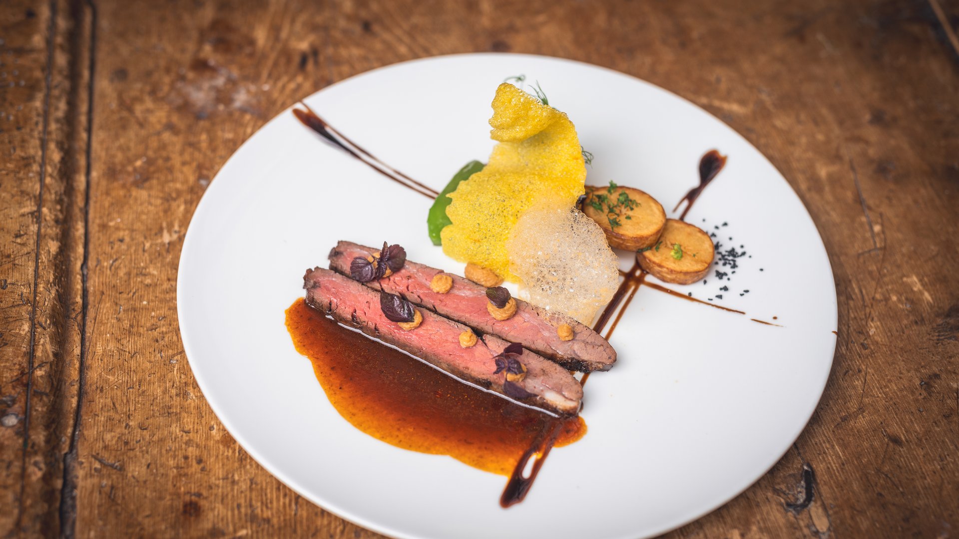 Gourmetgericht mit Fleisch, Kartoffeln und dekorativem Schaum auf weißem Teller