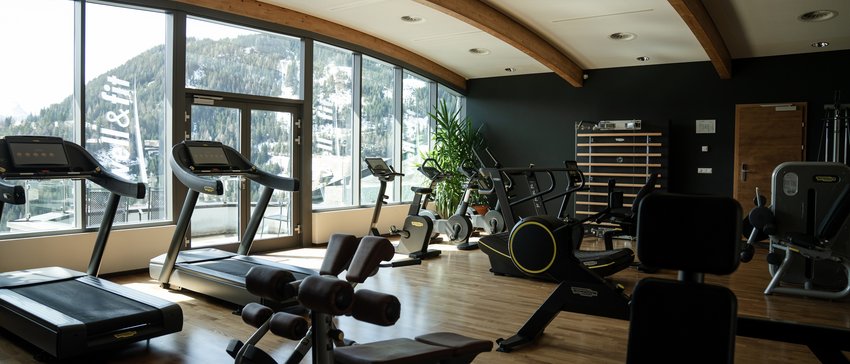 Fitnessraum mit Heimtrainern vor Fenstern mit Bergblick
