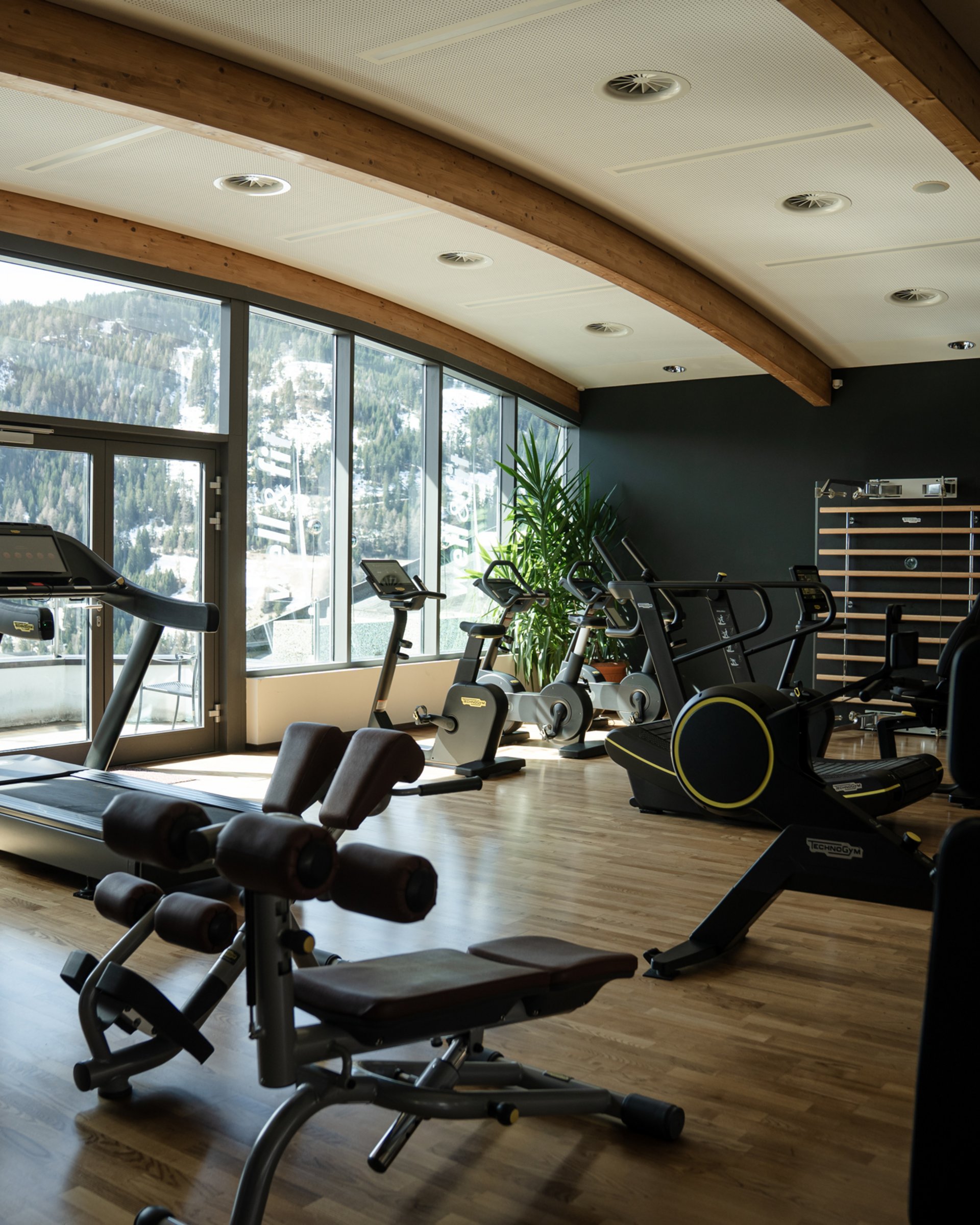 Fitnessraum mit Heimtrainern vor Fenstern mit Bergblick