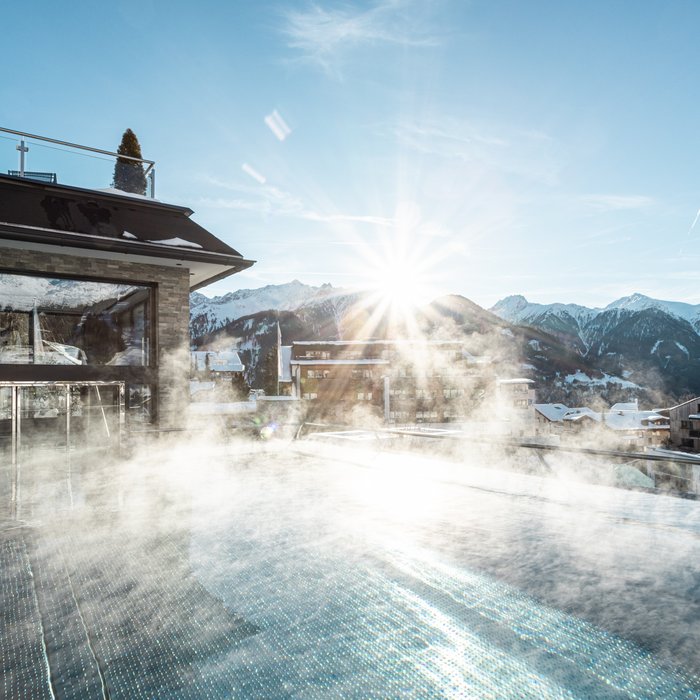 Dampfender Außenpool mit Bergblick bei Sonnenaufgang in winterlicher Landschaft