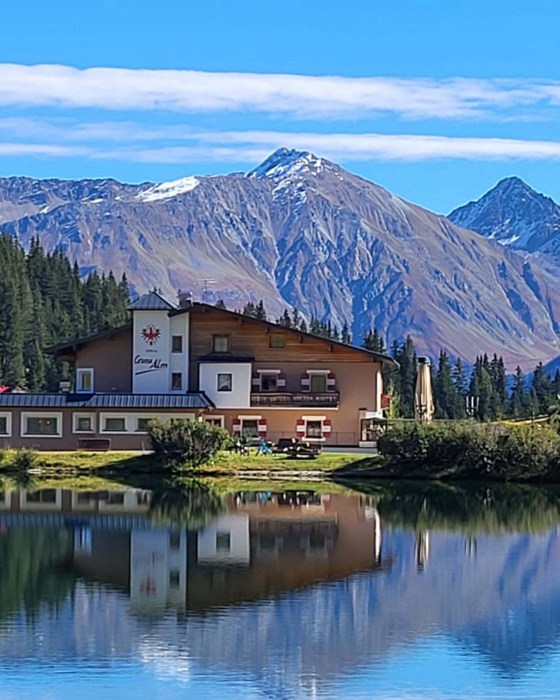 Die Cervosa Alm auf 2 000 Metern Haus am See mit Wald und Bergen im klaren blauen Himmel