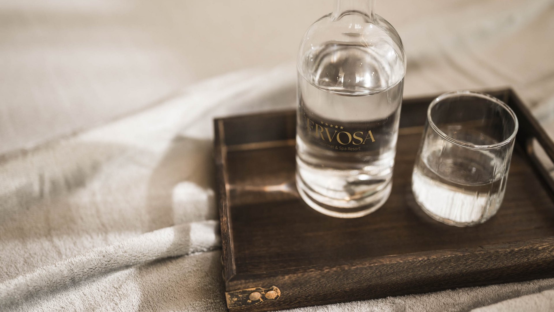 Water bottle and glass on a wooden tray on soft fabric