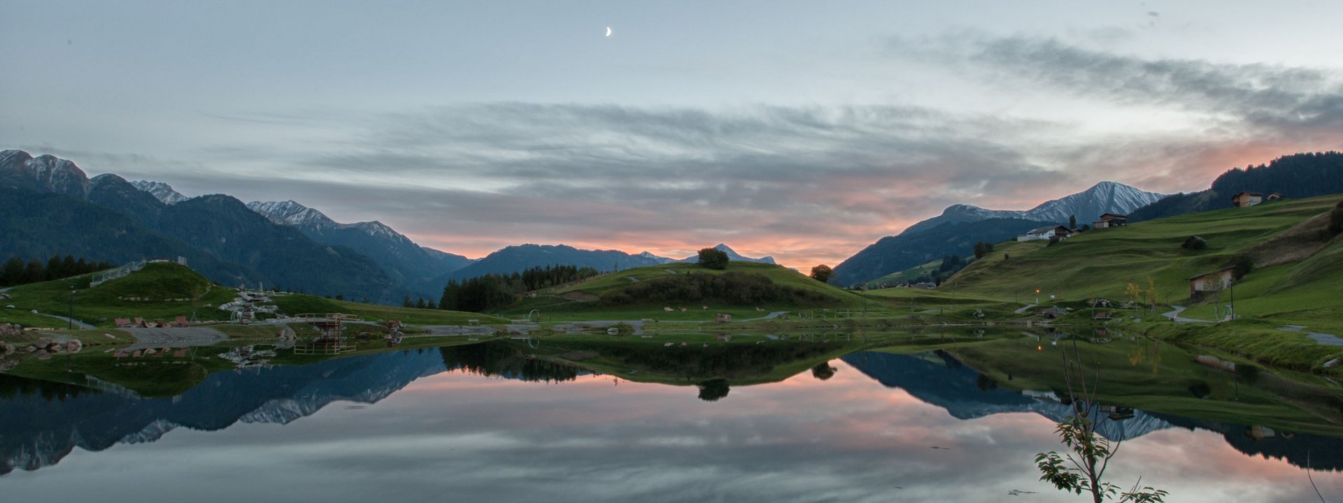 Bergsee spiegelt Hügel und Mond in ruhiger Abenddämmerung