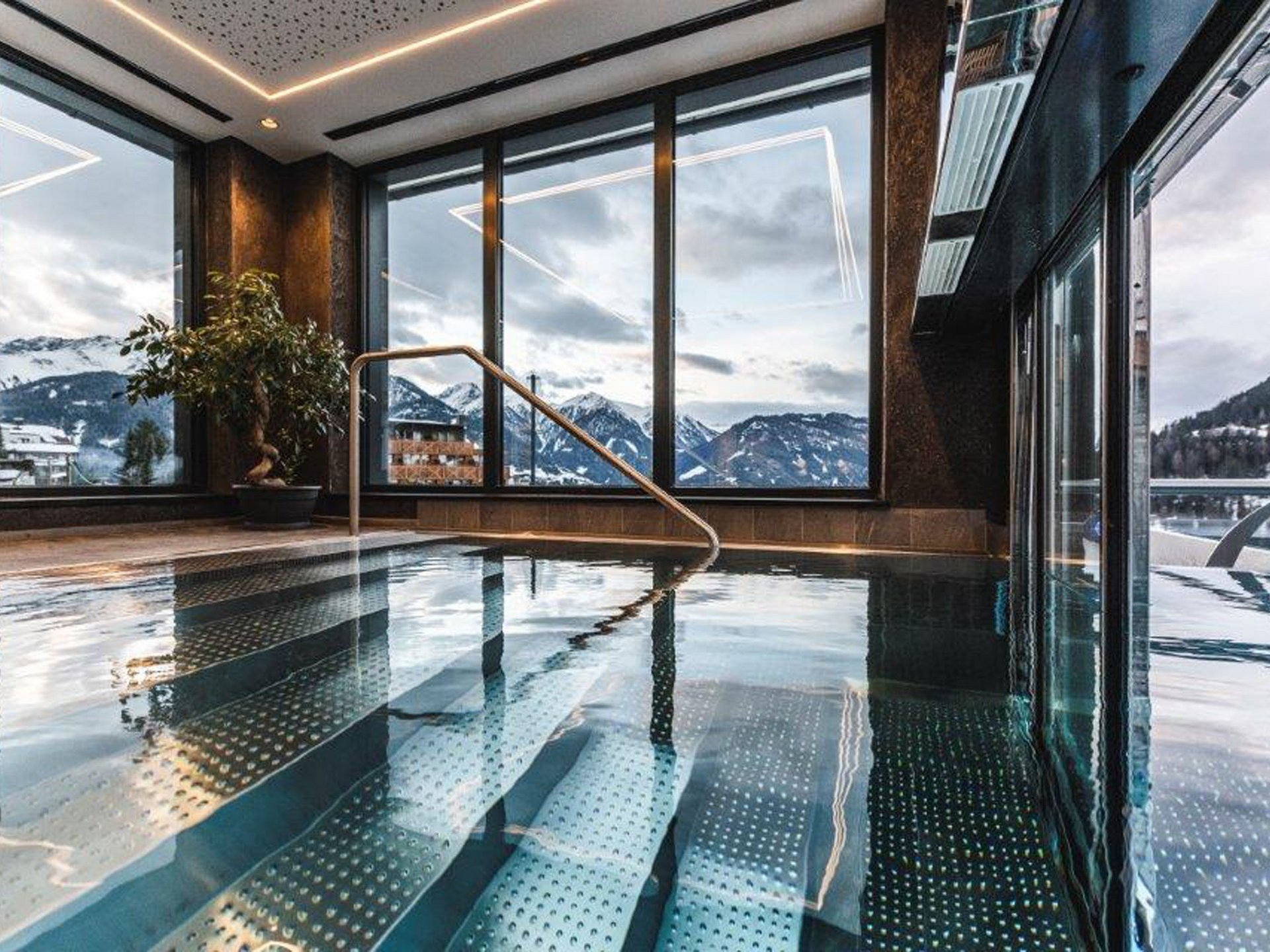 Wohlfühlurlaub im 5-Sterne-Hotel in Serfaus Innenpool mit Panoramafenstern und Blick auf verschneite Berge