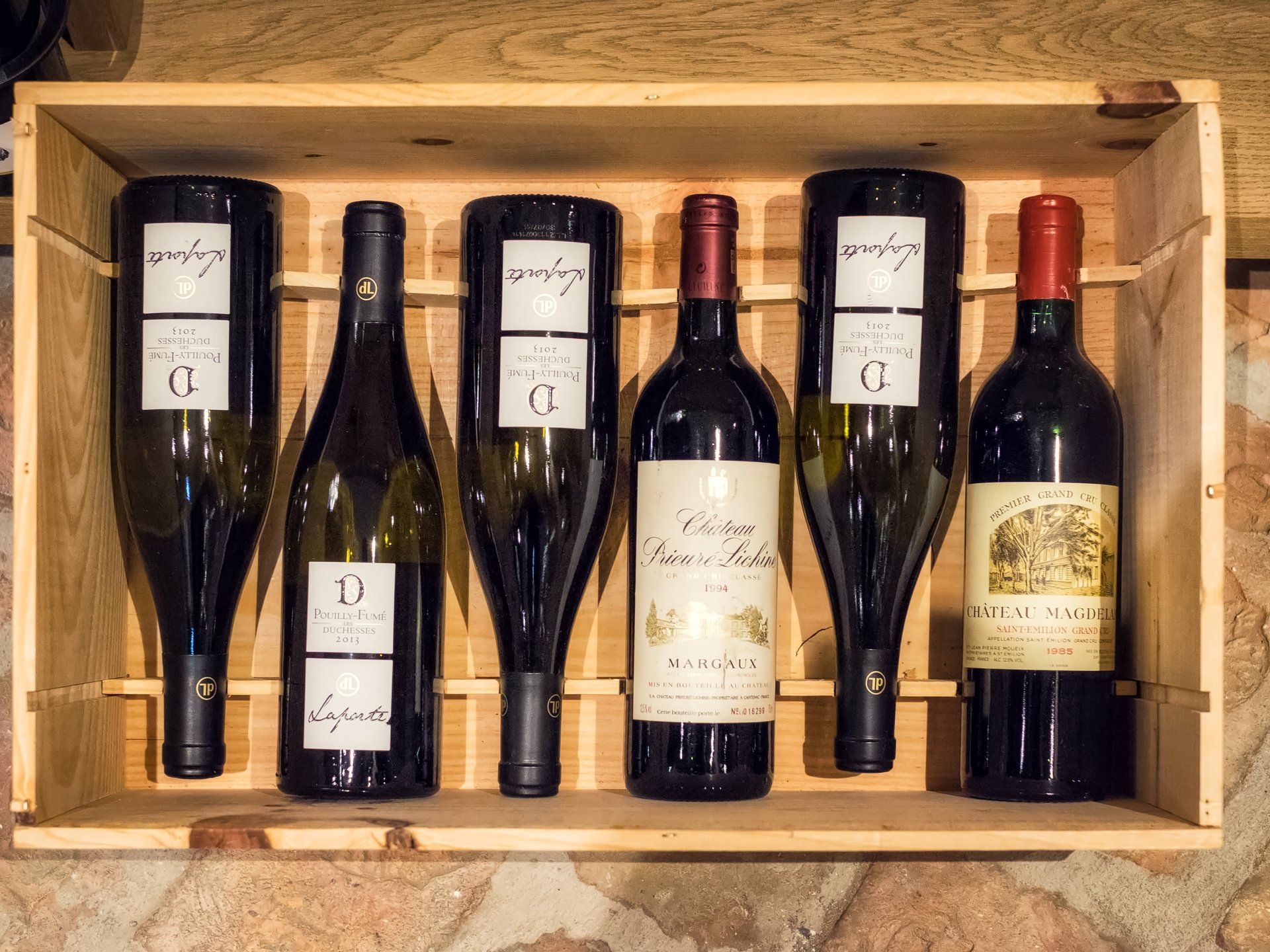Six wine bottles in a wooden crate on a stone floor