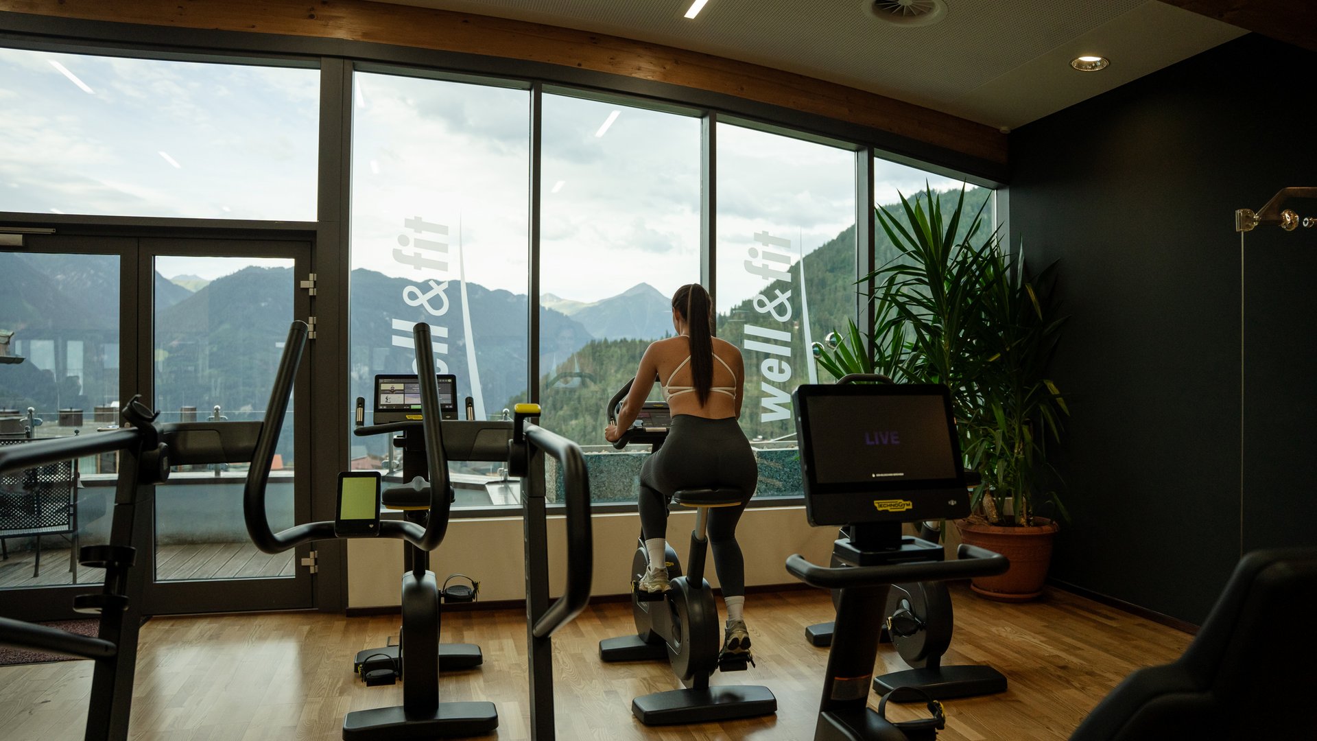 Woman exercising on stationary bike by large window with mountain view in gym