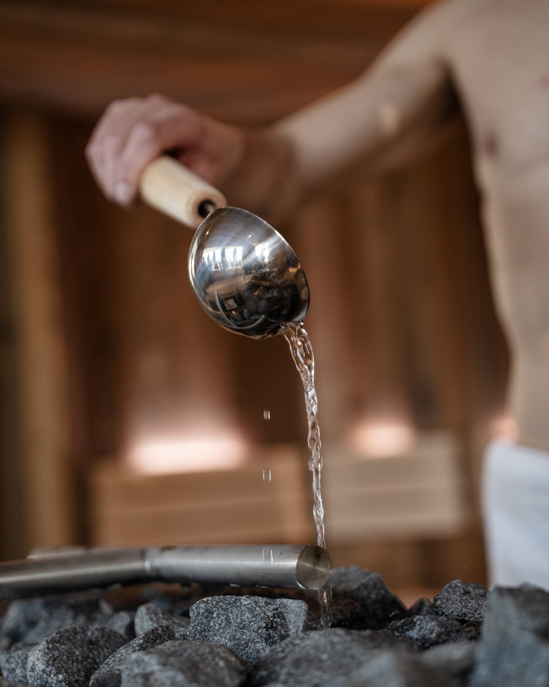 Wasser wird mit Kelle über heiße Steine in Sauna gegossen