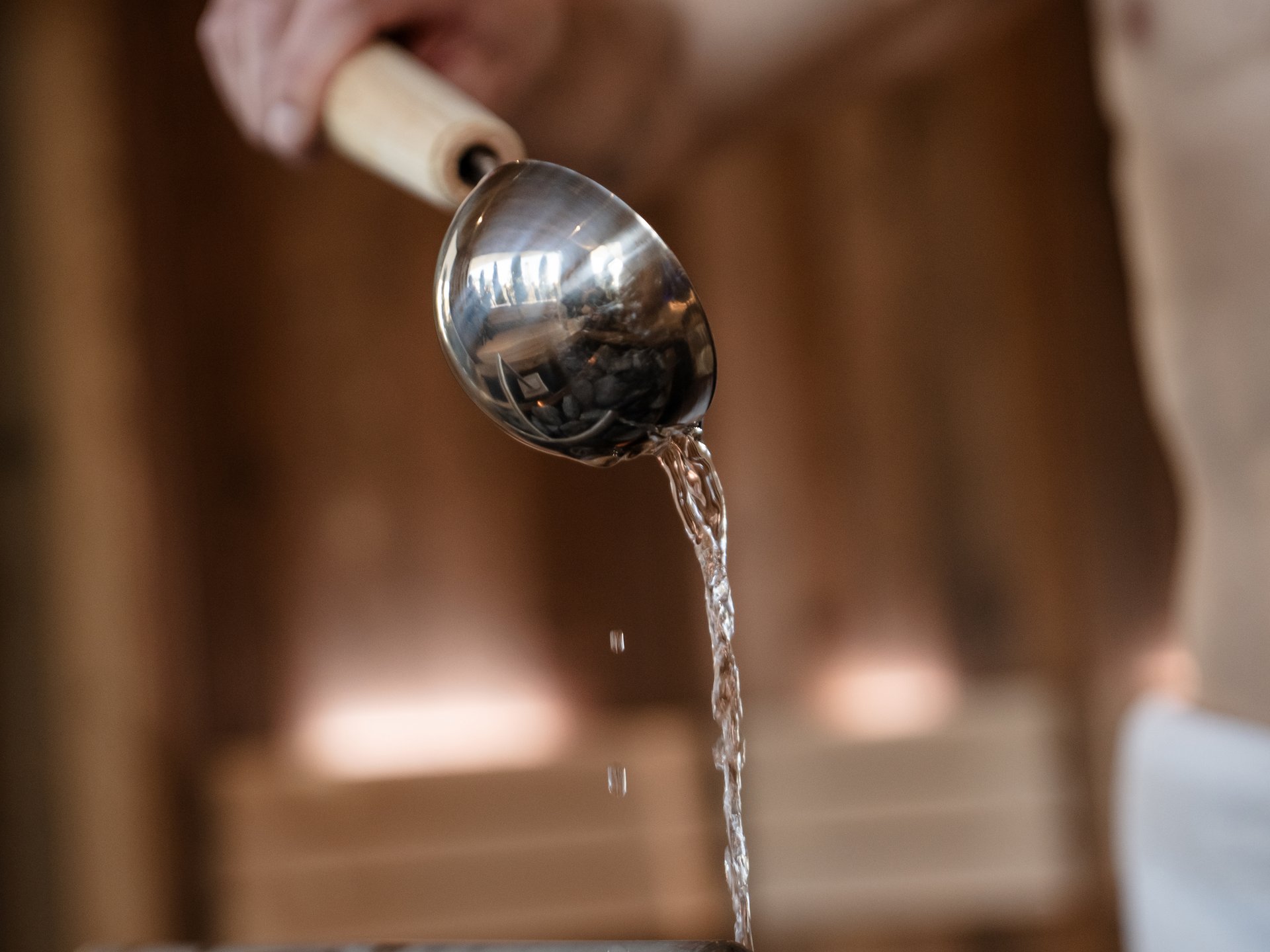 Wasser wird mit Kelle über heiße Steine in Sauna gegossen