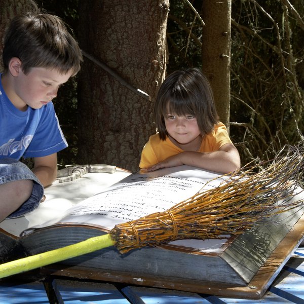 Zwei Kinder lesen ein großes Buch im Wald neben einem Besen
