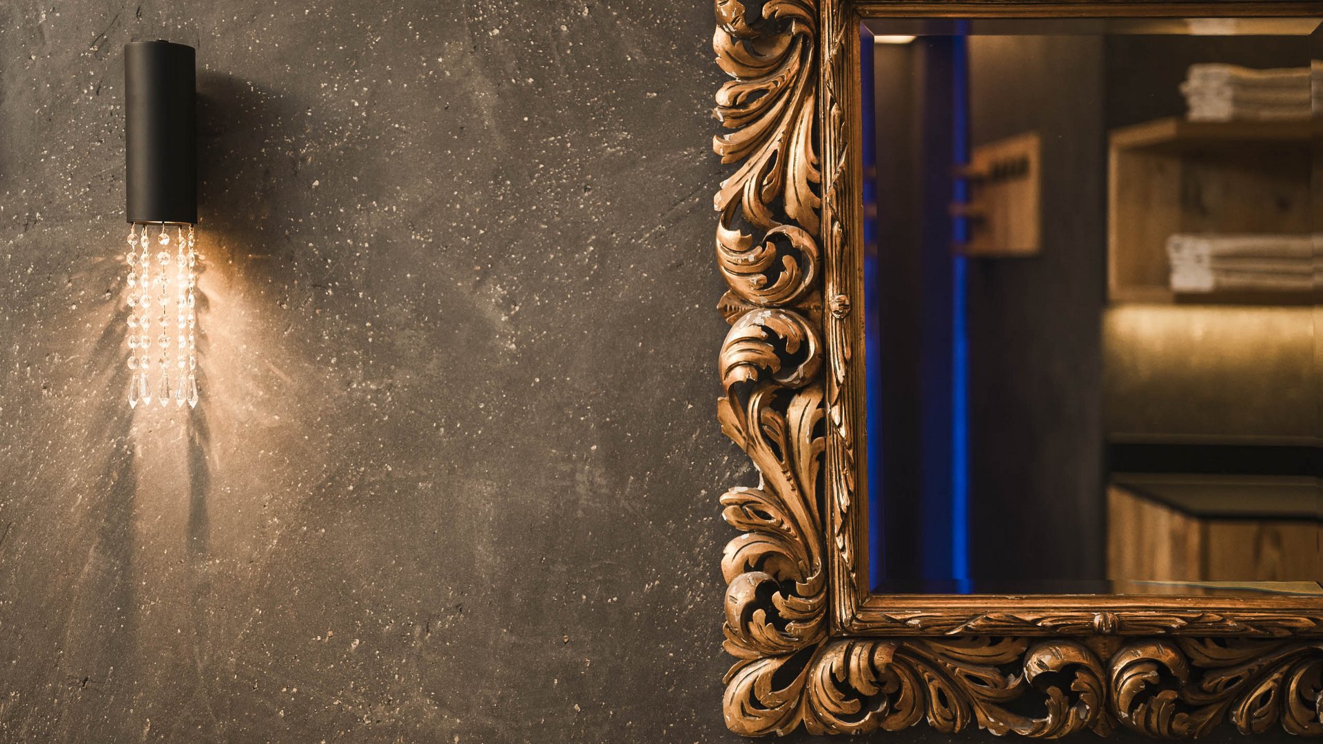 Wall lamp beside ornate mirror frame on a gray wall