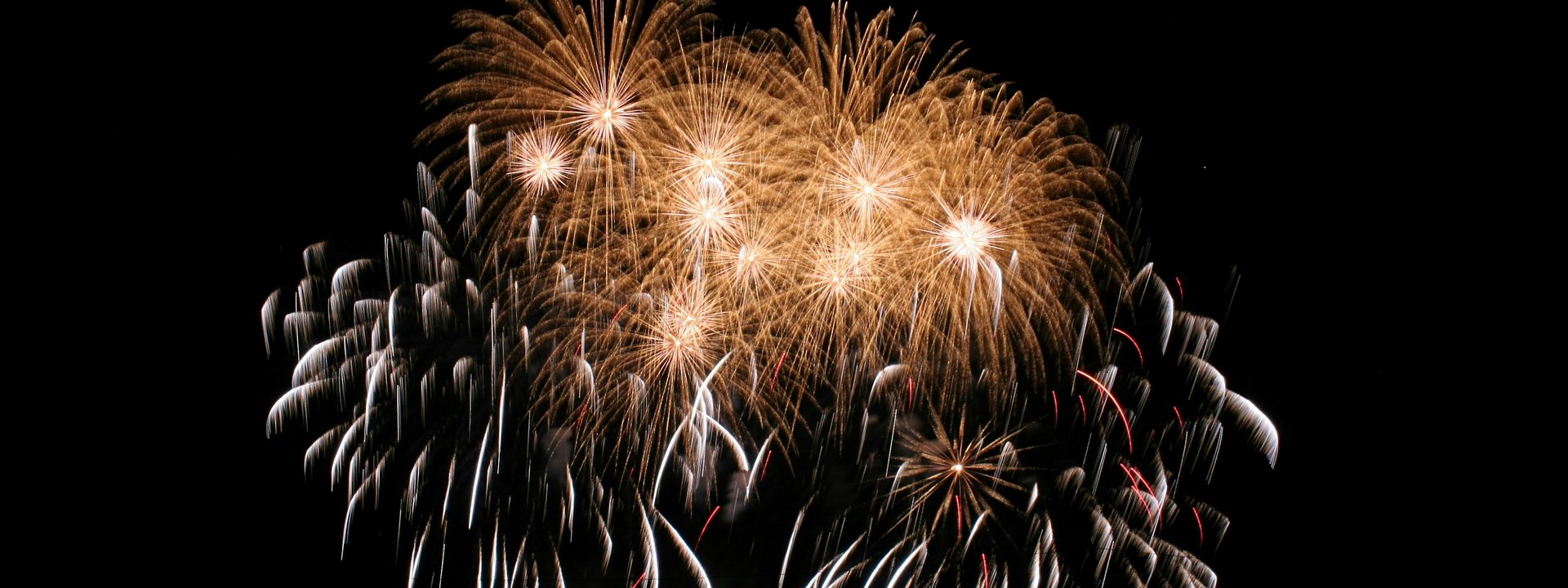 Goldene und weiße Feuerwerkskörper leuchten am Nachthimmel