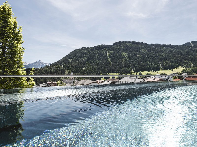 Infinity-Pool mit Aussicht auf grüne Berge und Dorf bei klarem Himmel