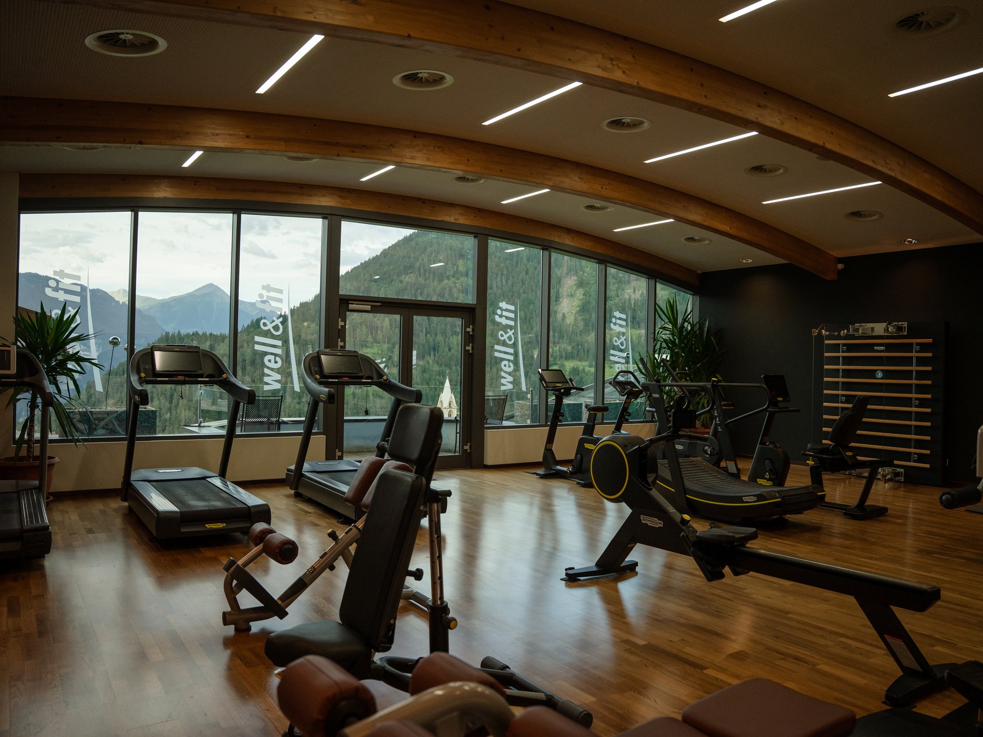 Bewegung im Sporthotel mit Fitnessstudio Fitnessraum mit Geräten und großen Fenstern mit Bergblick