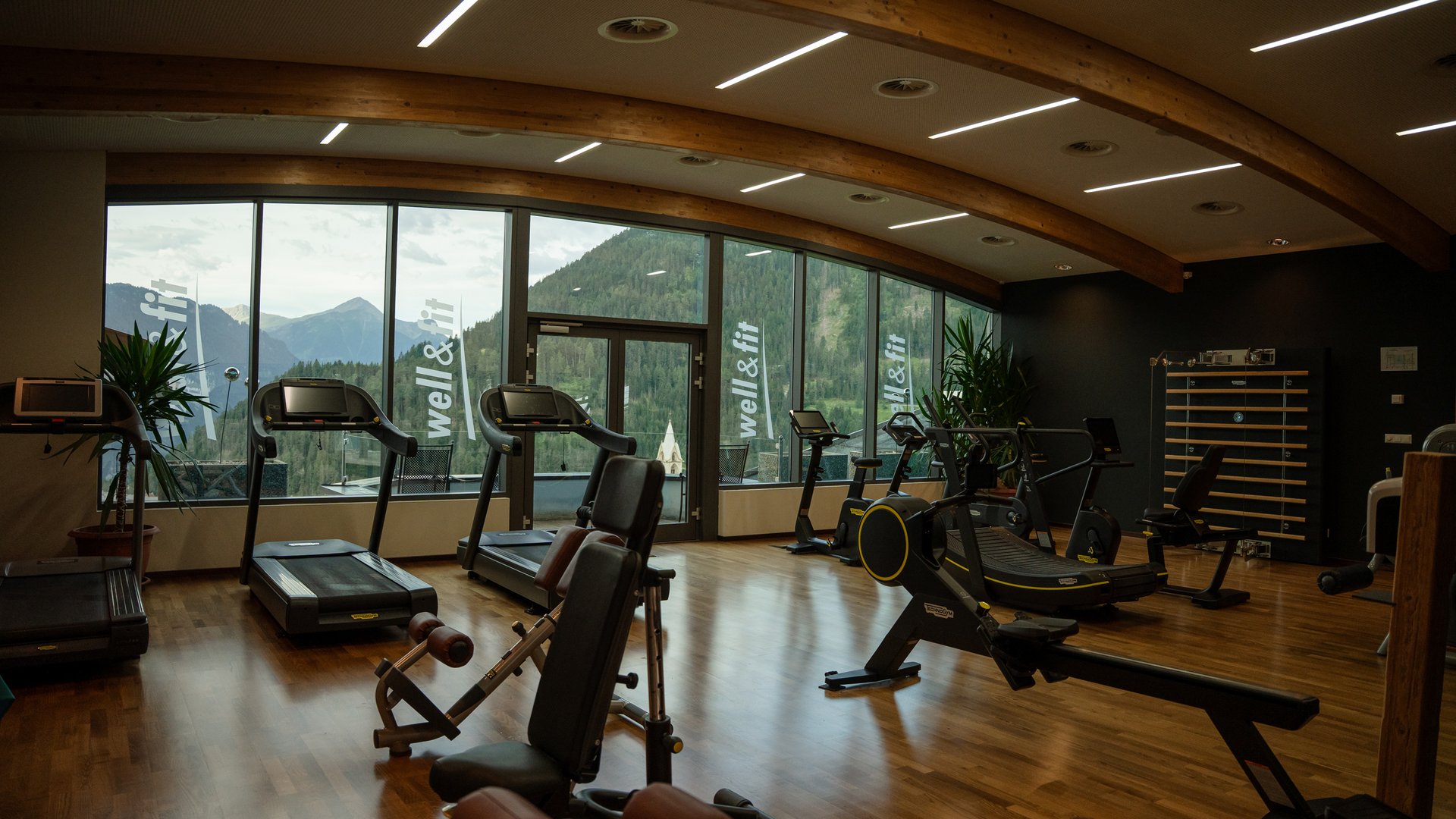 Bewegung im Sporthotel mit Fitnessstudio Fitnessraum mit Geräten und großen Fenstern mit Bergblick