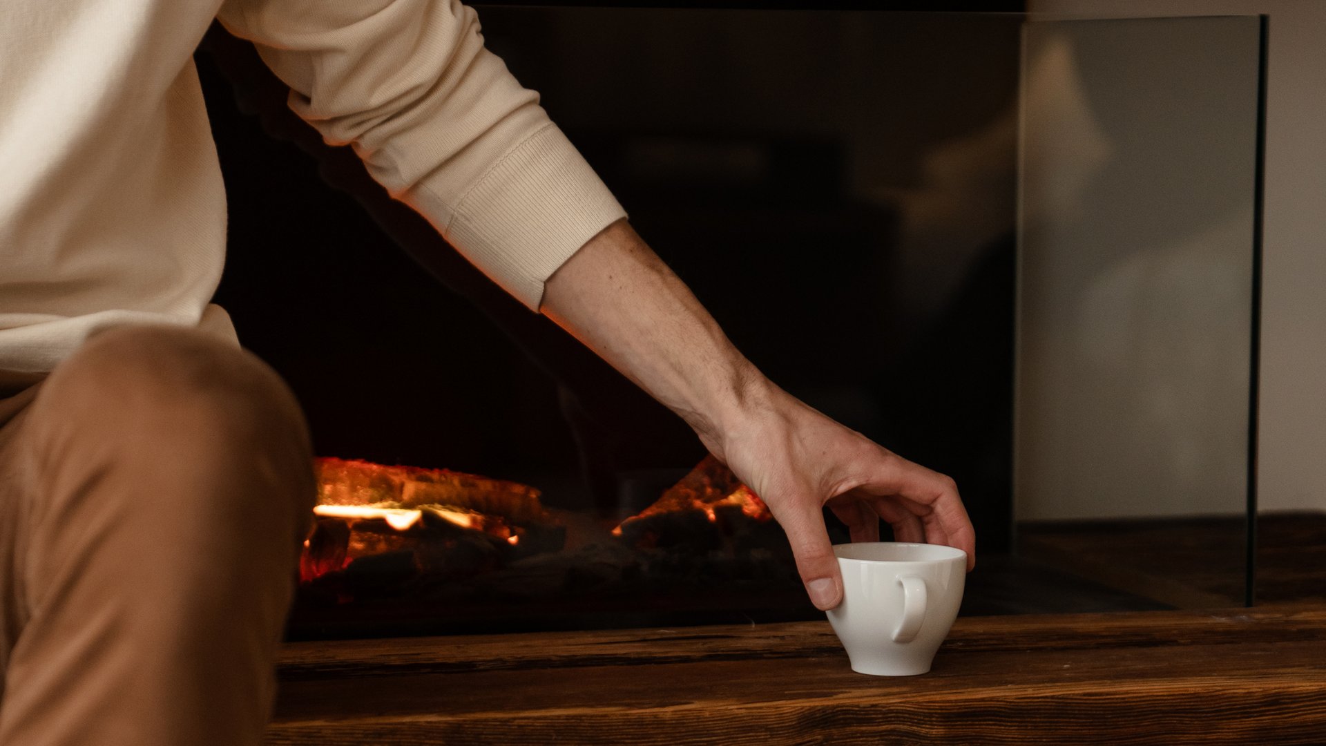 Person reaches for cup near modern electric fireplace