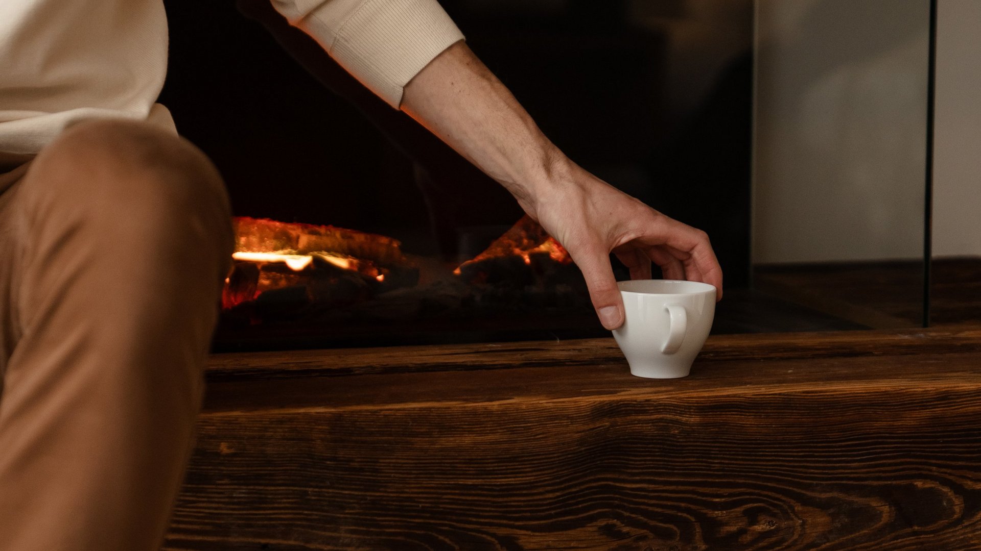Person greift nach Tasse vor einem modernen elektrischen Kamin