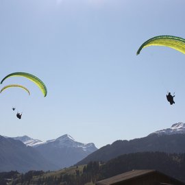 Drei Gleitschirmflieger über Bergen mit blauem Himmel