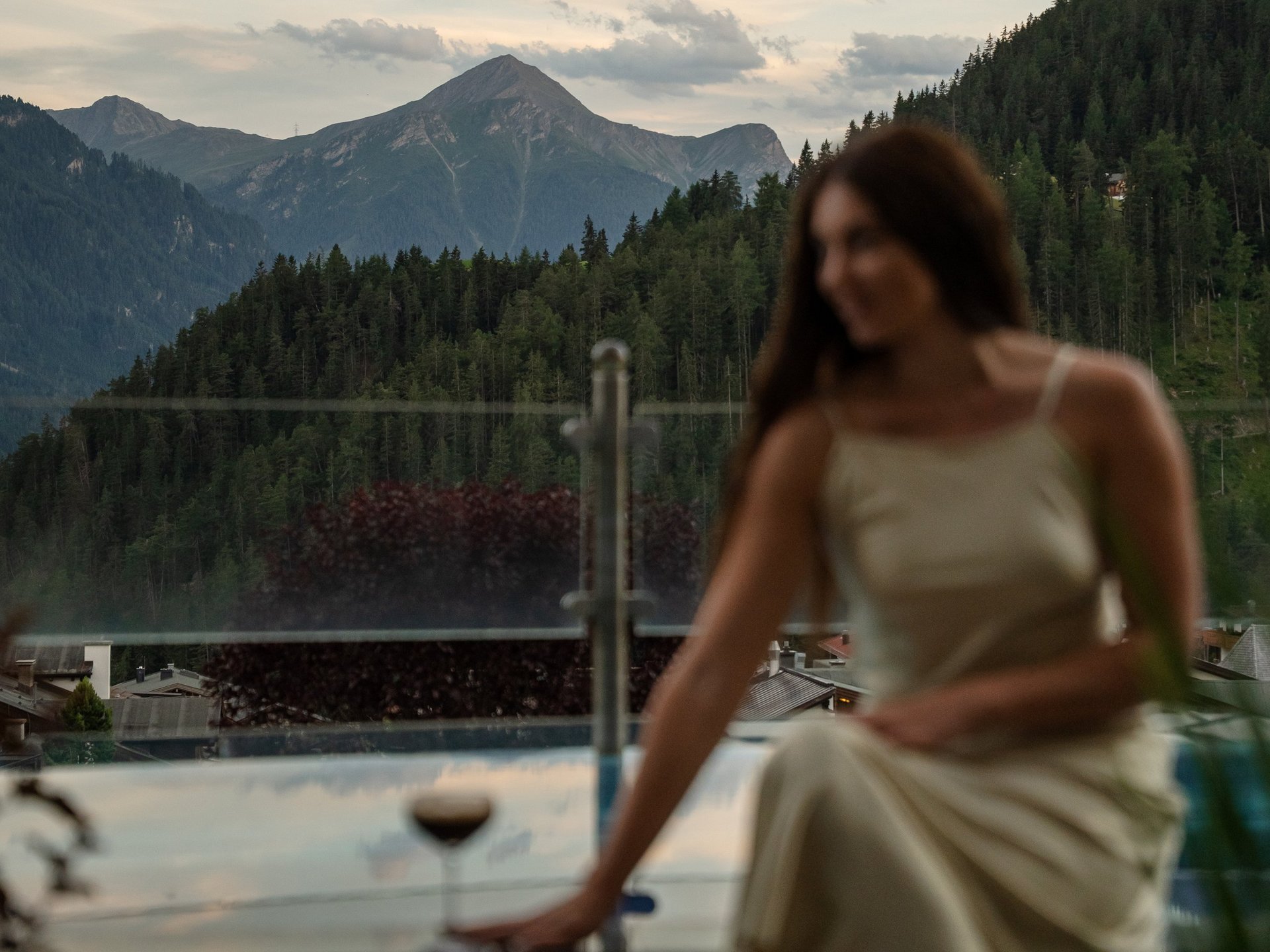 Hochgenuss in flüssiger Form Frau in Kleid sitzt neben Pool mit Bergblick bei Sonnenuntergang