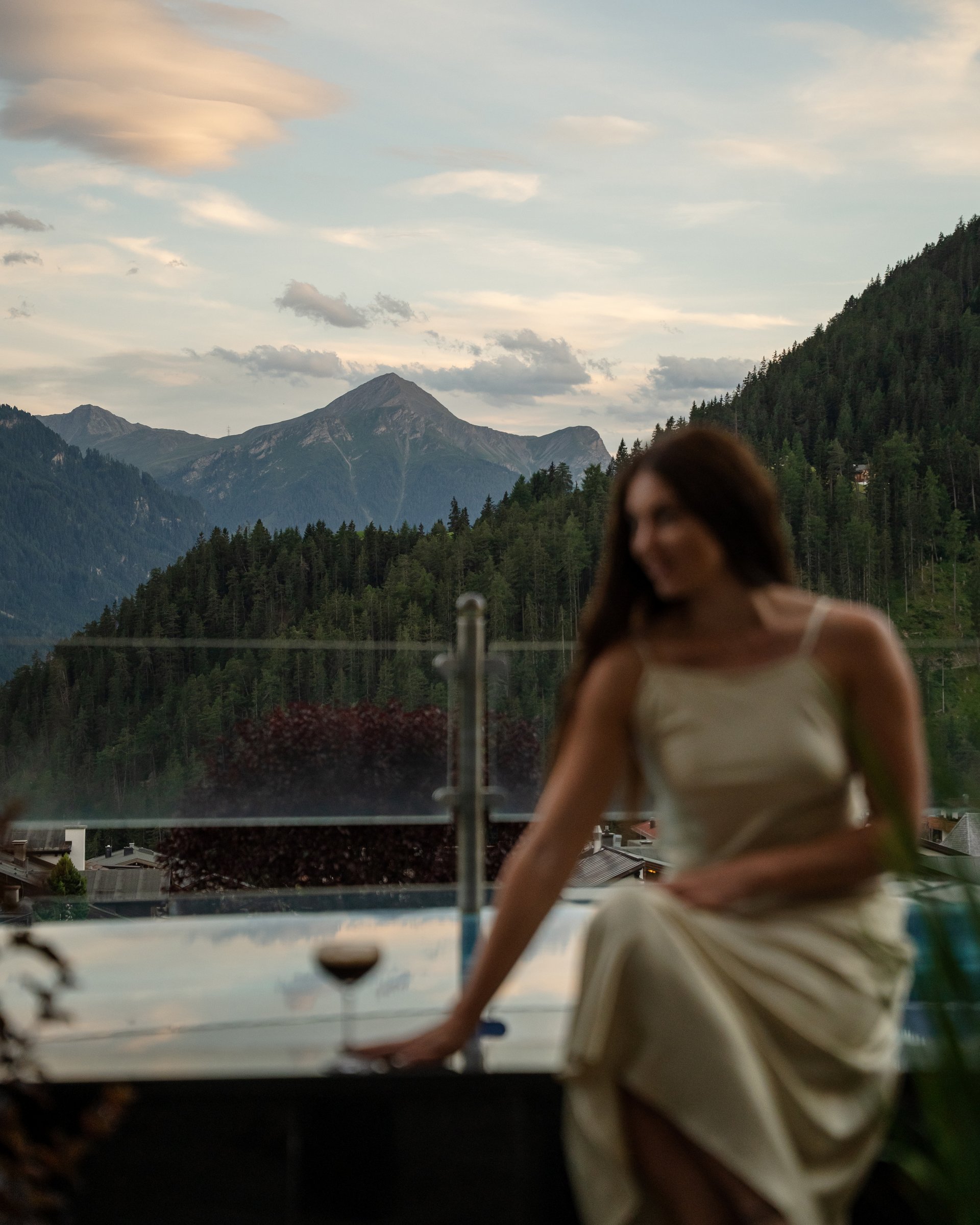 Feel-good holiday at our 5-star hotel in Serfaus Woman in dress sitting by pool with mountain view at sunset