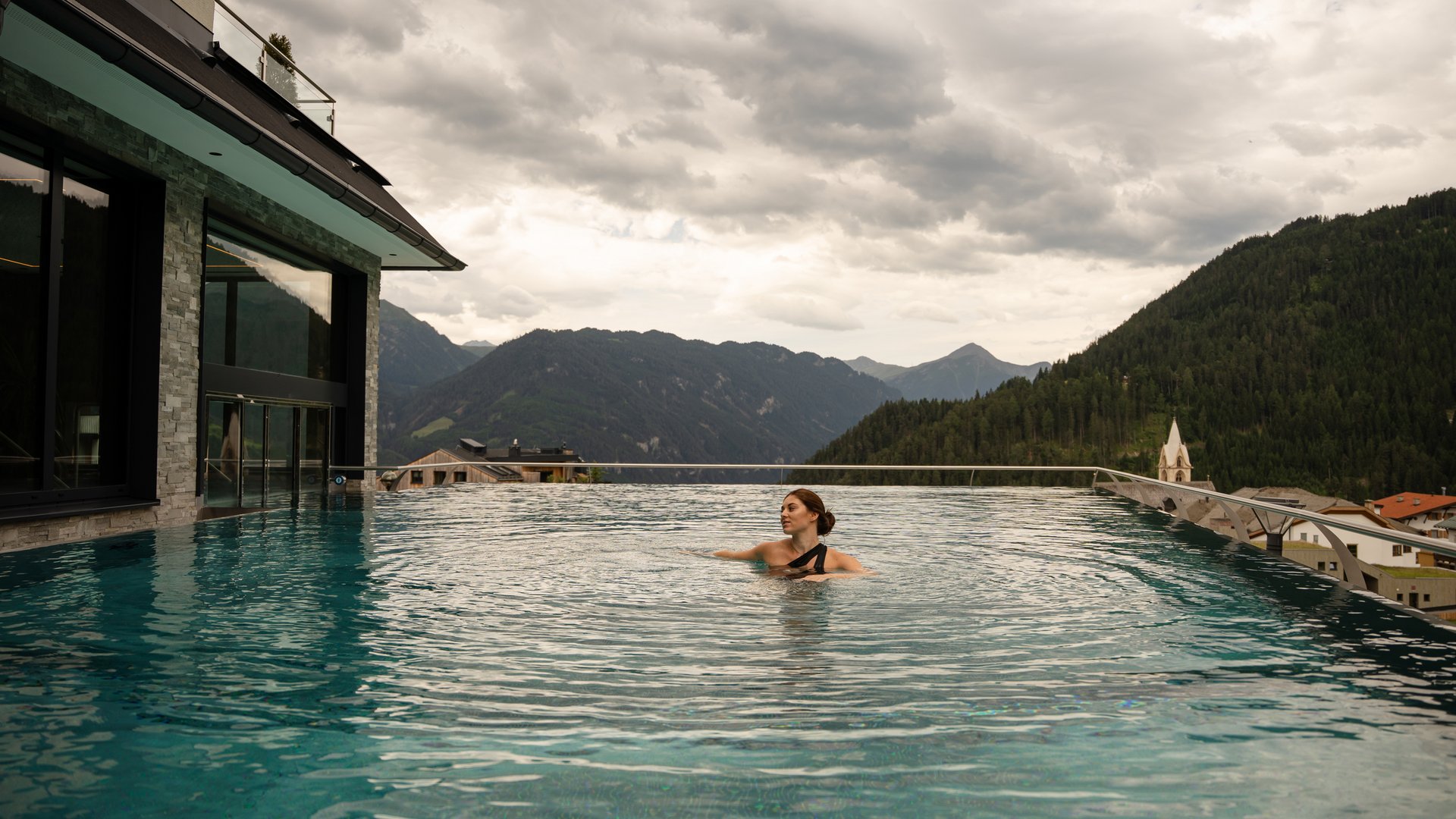 Woman relaxing in infinity pool with mountain view and cloudy sky