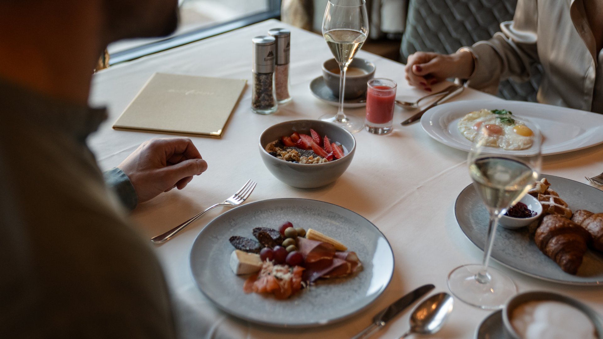 Breakfast table with various dishes, drinks, and two people dining in a restaurant
