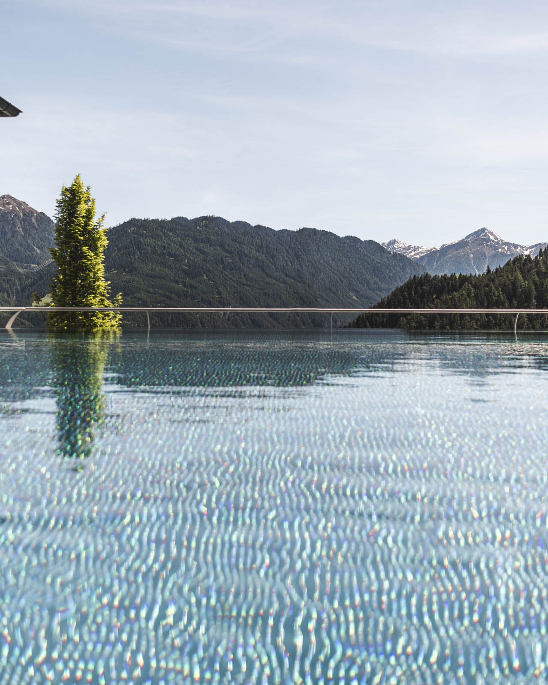 Infinity pool overlooking mountainous landscape with trees and snow-capped peaks